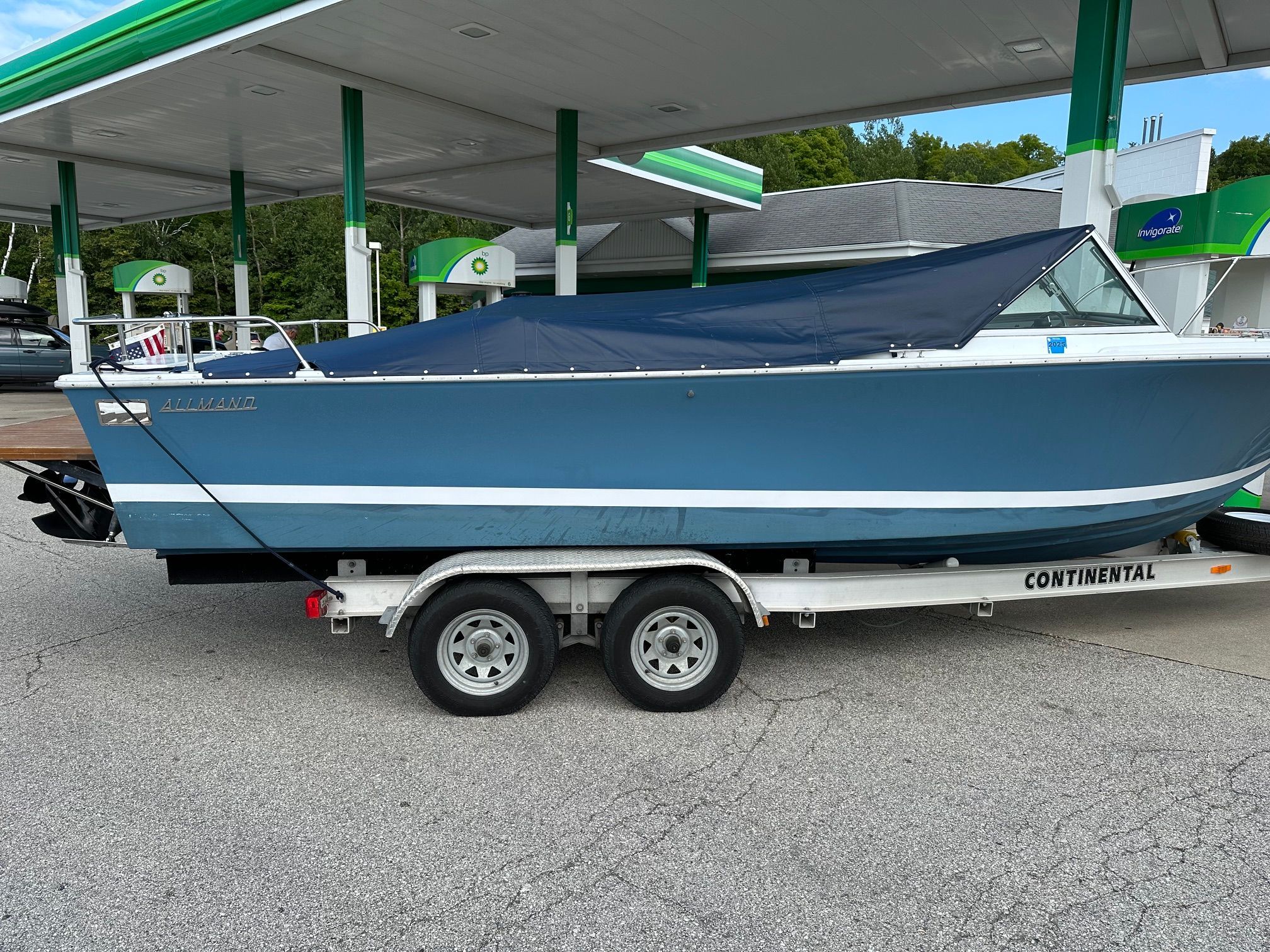 A blue 1969 John Allmand Citation II on a trailer at a gas station.