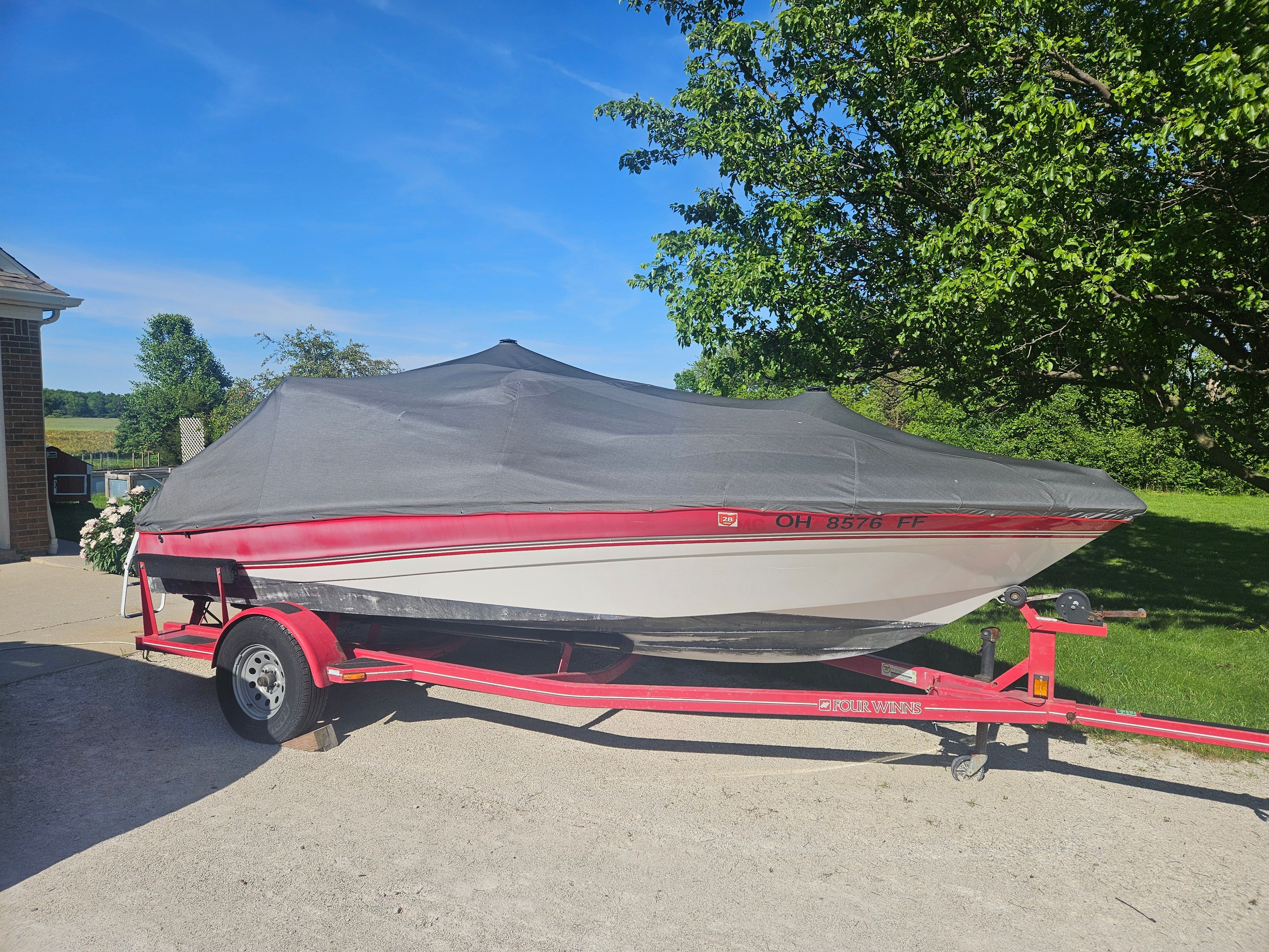 A 1997 Four Winns Horizon boat on a trailer, covered, parked in a driveway.