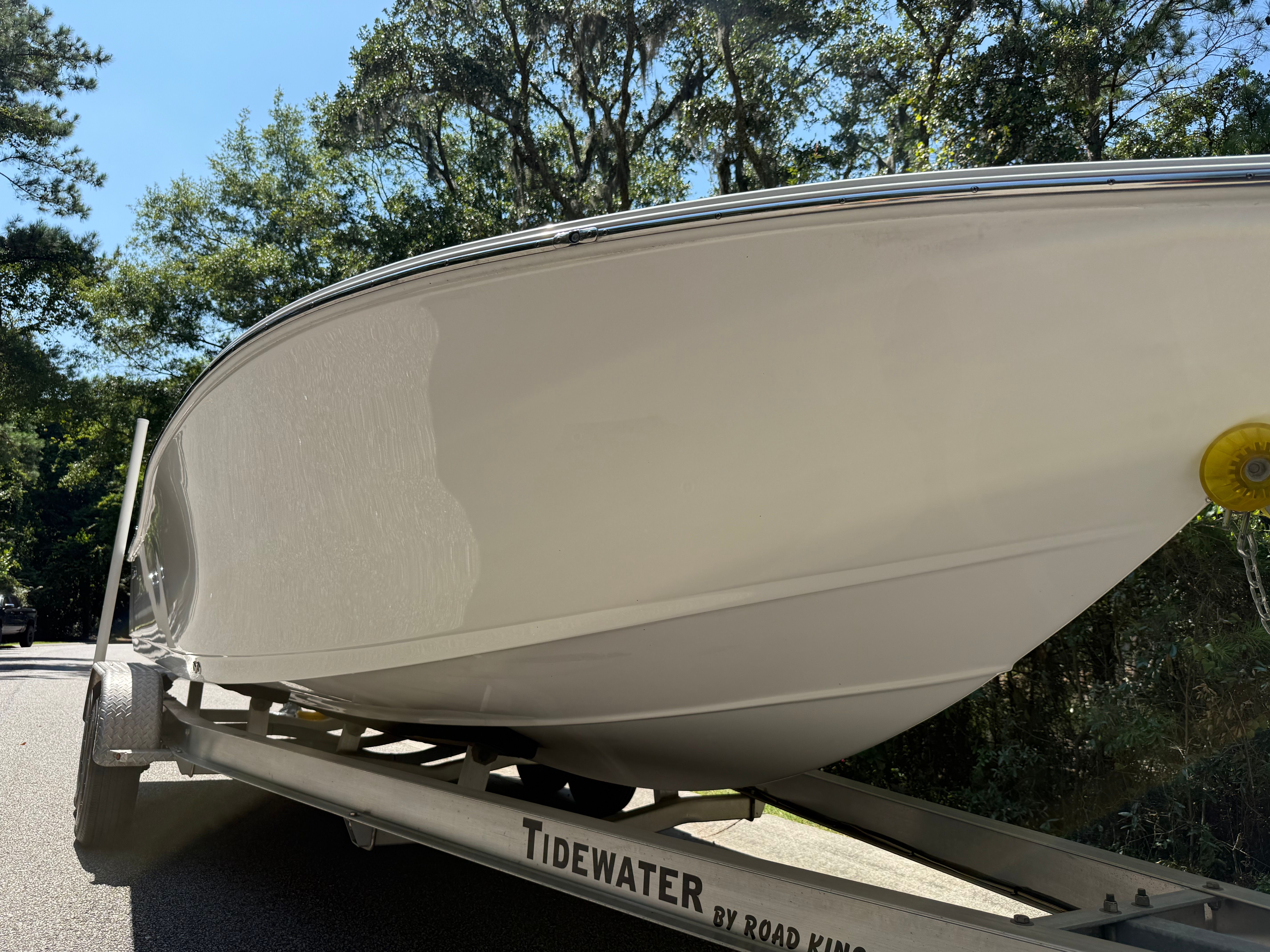 A Tidewater 2210 Carolina Bay boat on a trailer, surrounded by trees.