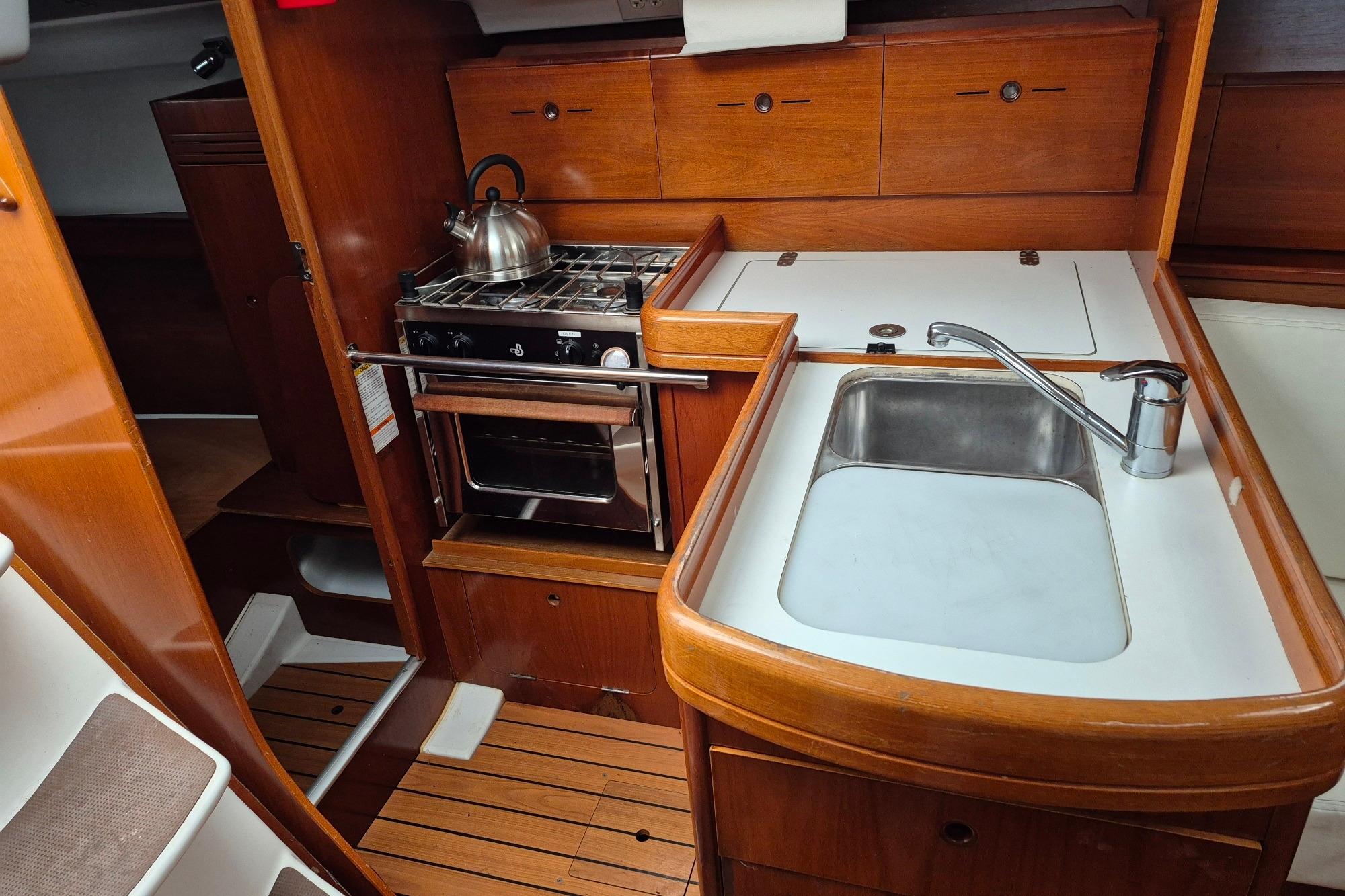 2003 Beneteau First 36.7 yacht kitchen with stove, sink, and wooden cabinetry.