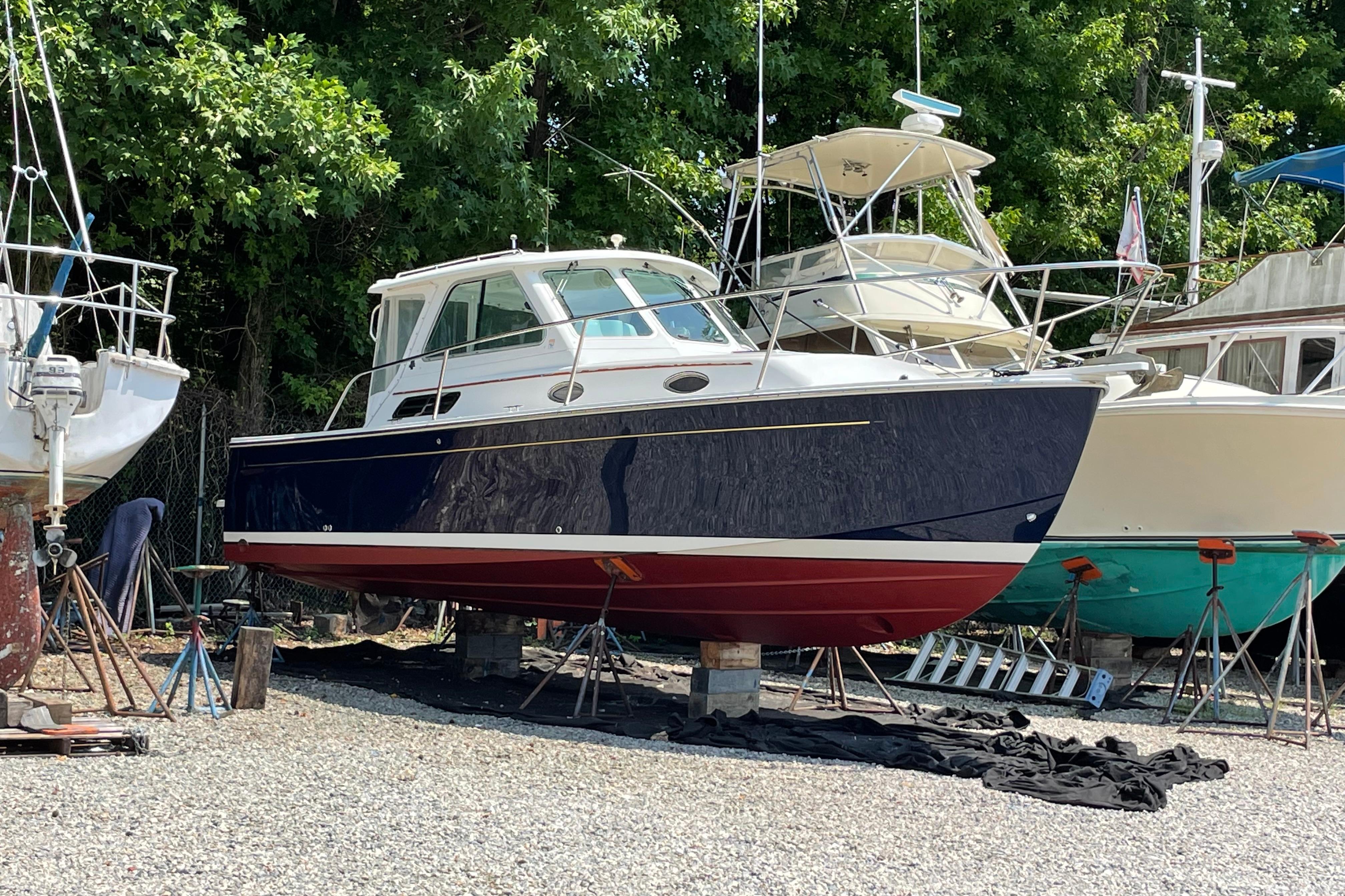 2007 Back Cove 29 boat on stands in a boatyard, surrounded by trees.