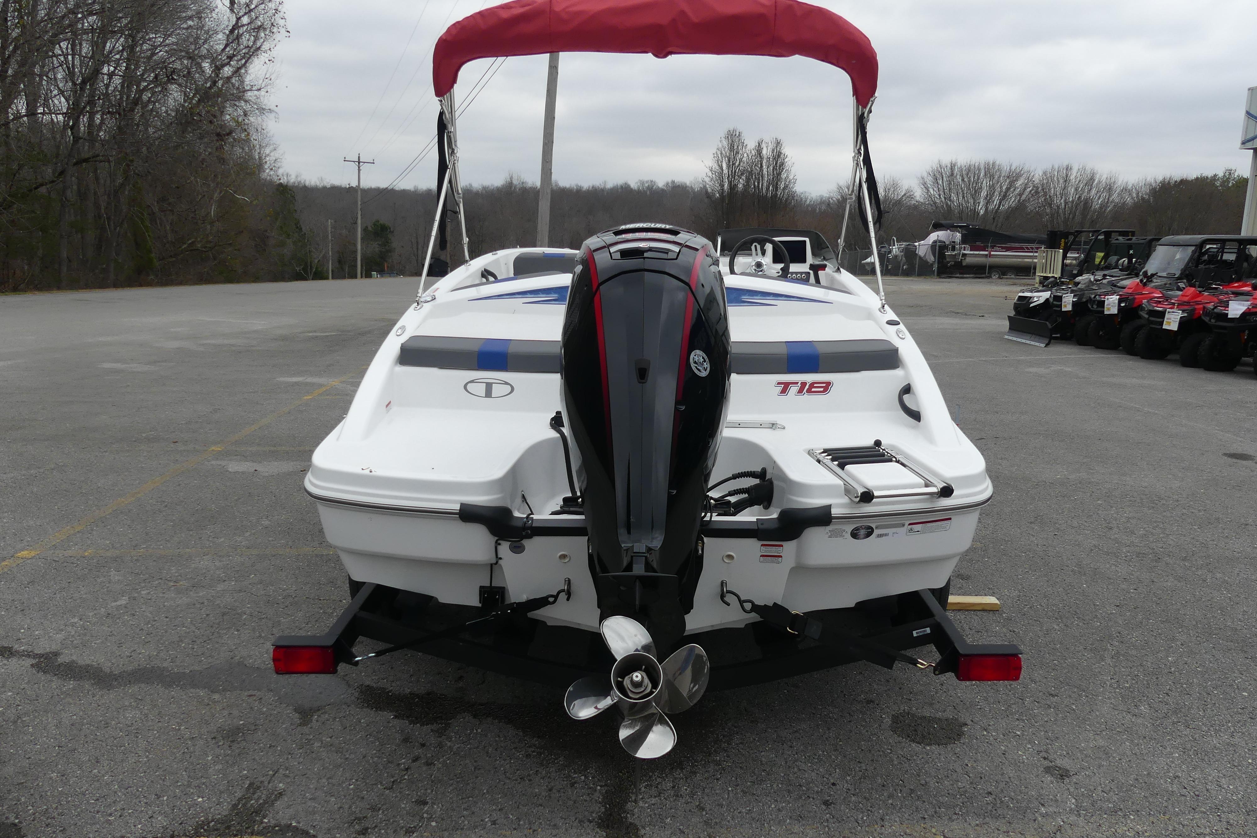 2024 Tahoe T18 boat with outboard motor and red canopy, parked on asphalt.