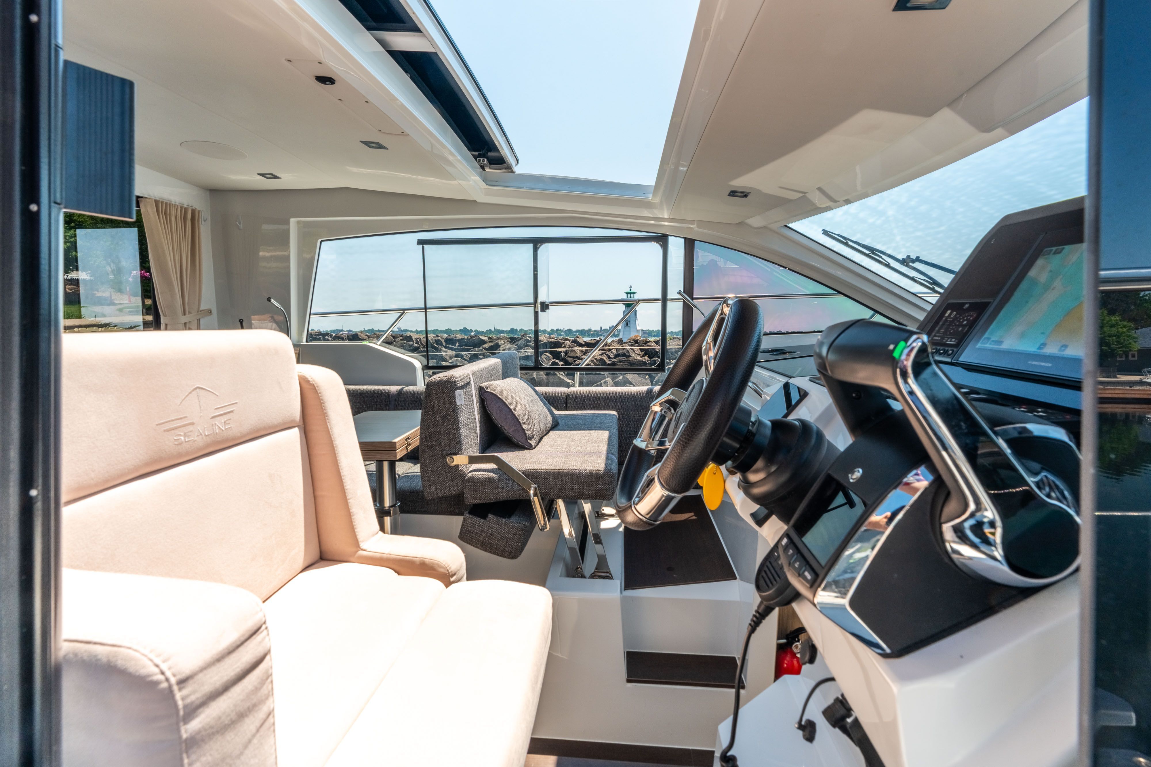 Interior of a modern yacht with comfortable seating and helm, overlooking the water.