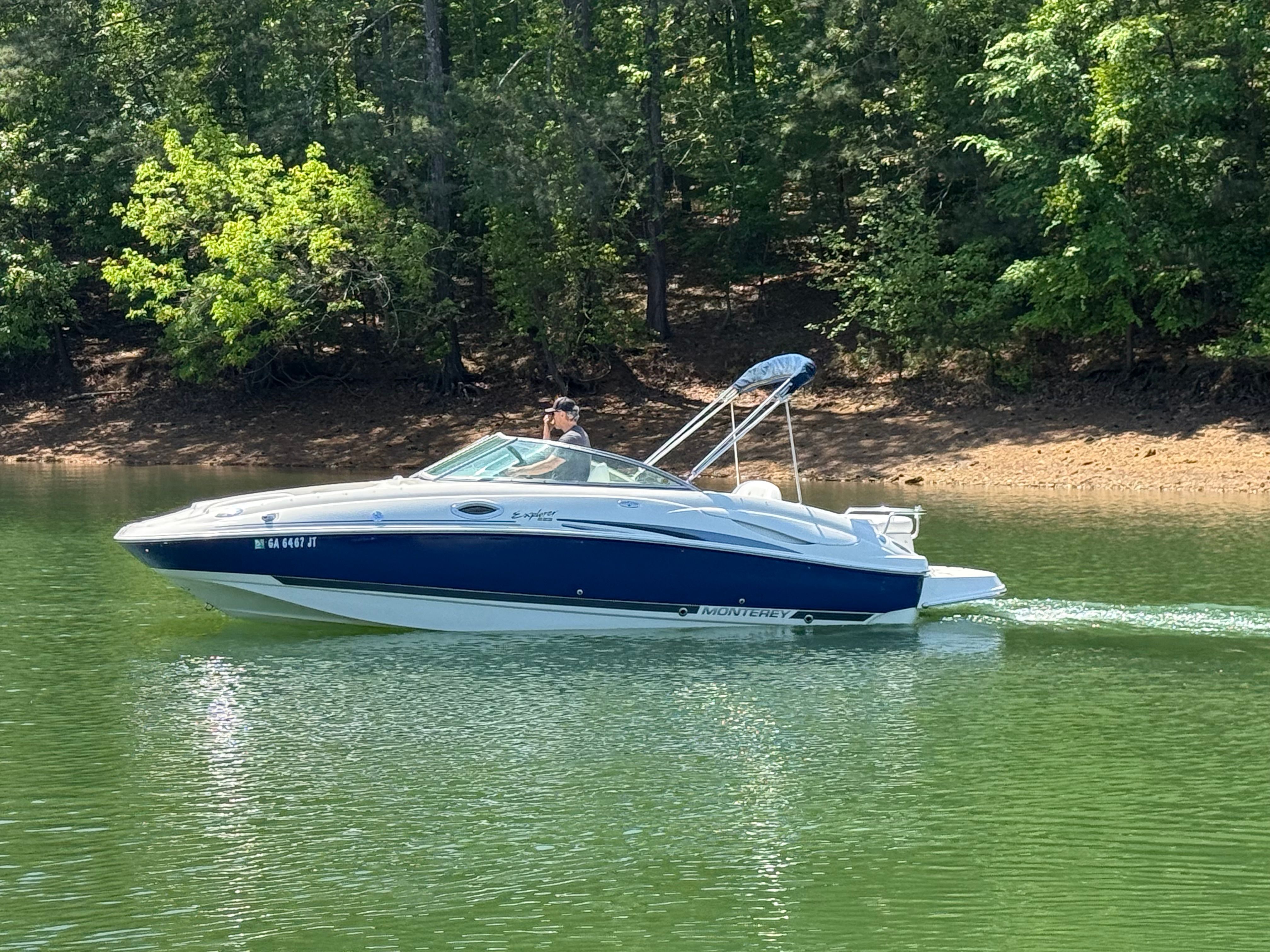 A white and blue 2005 Monterey 223 Explorer Sport boat cruising on a calm lake.
