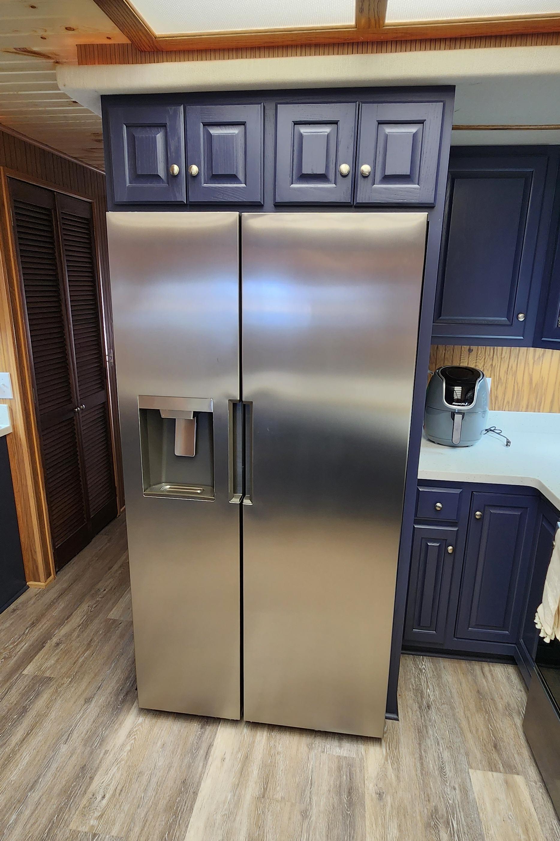 Stainless steel refrigerator in a modern kitchen with dark blue cabinets.