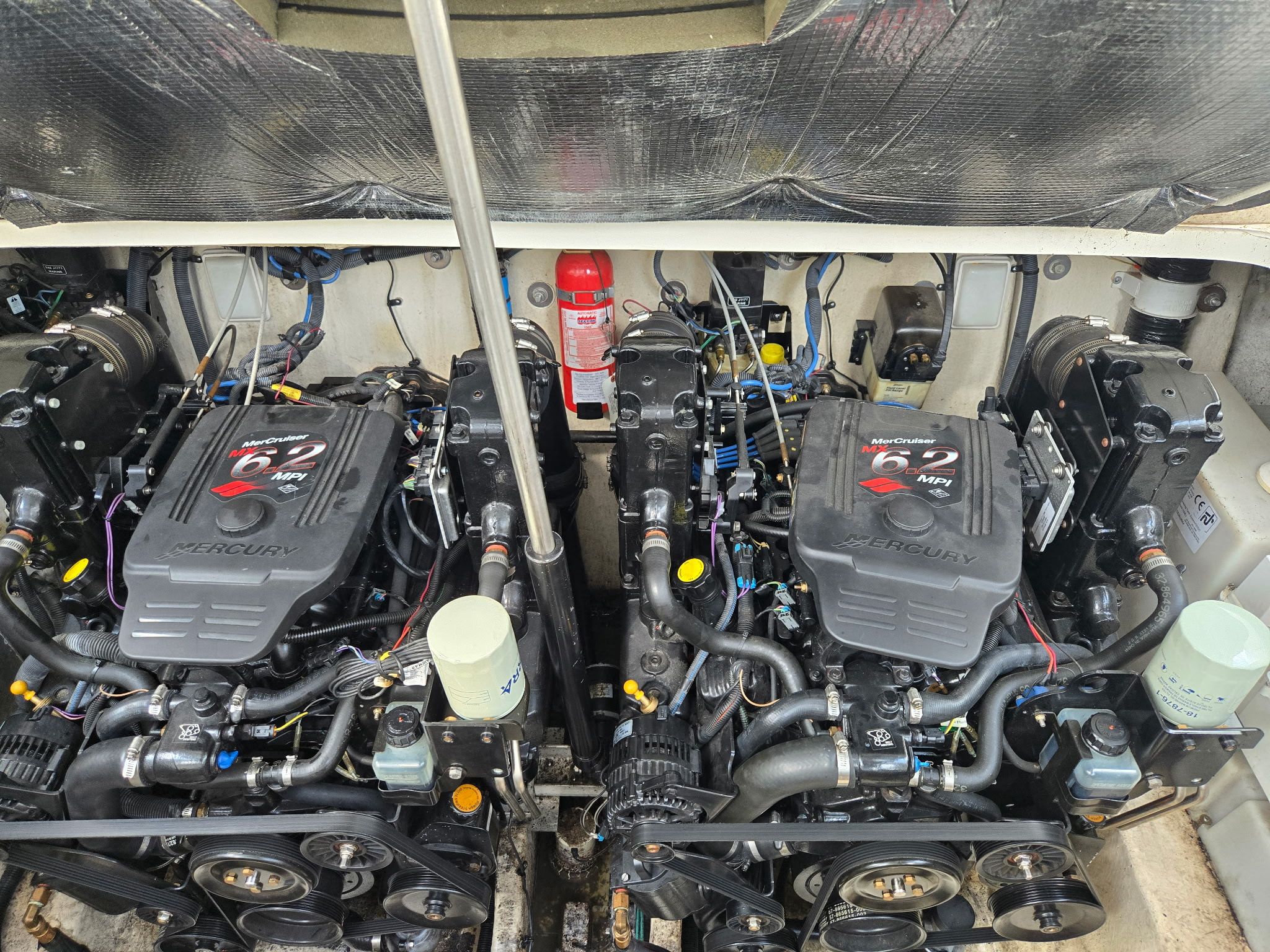 Two powerful engines in a boat's engine room, with a fire extinguisher in between.