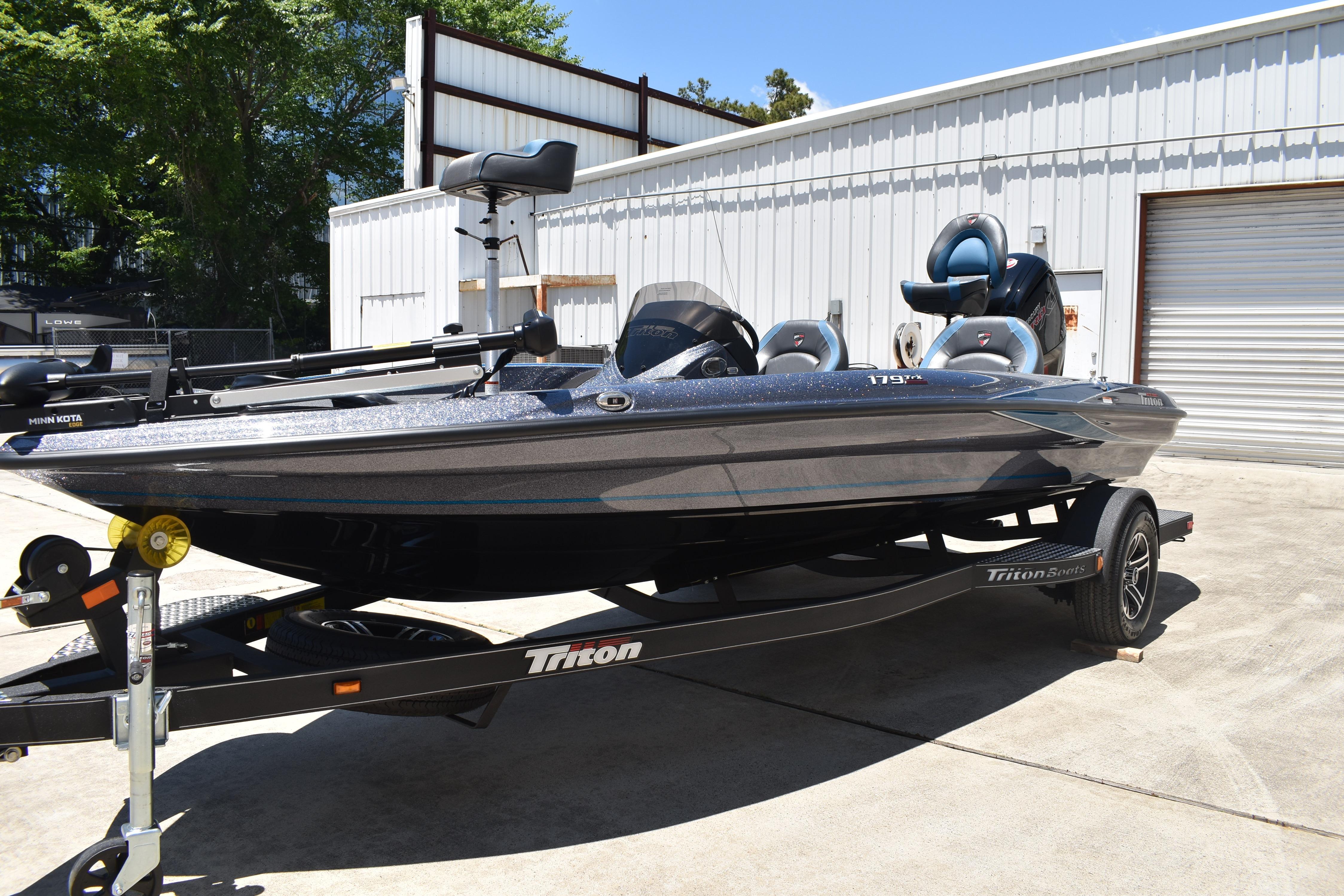 2026 Triton 179 TrX bass boat on trailer, parked outdoors near a metal building.