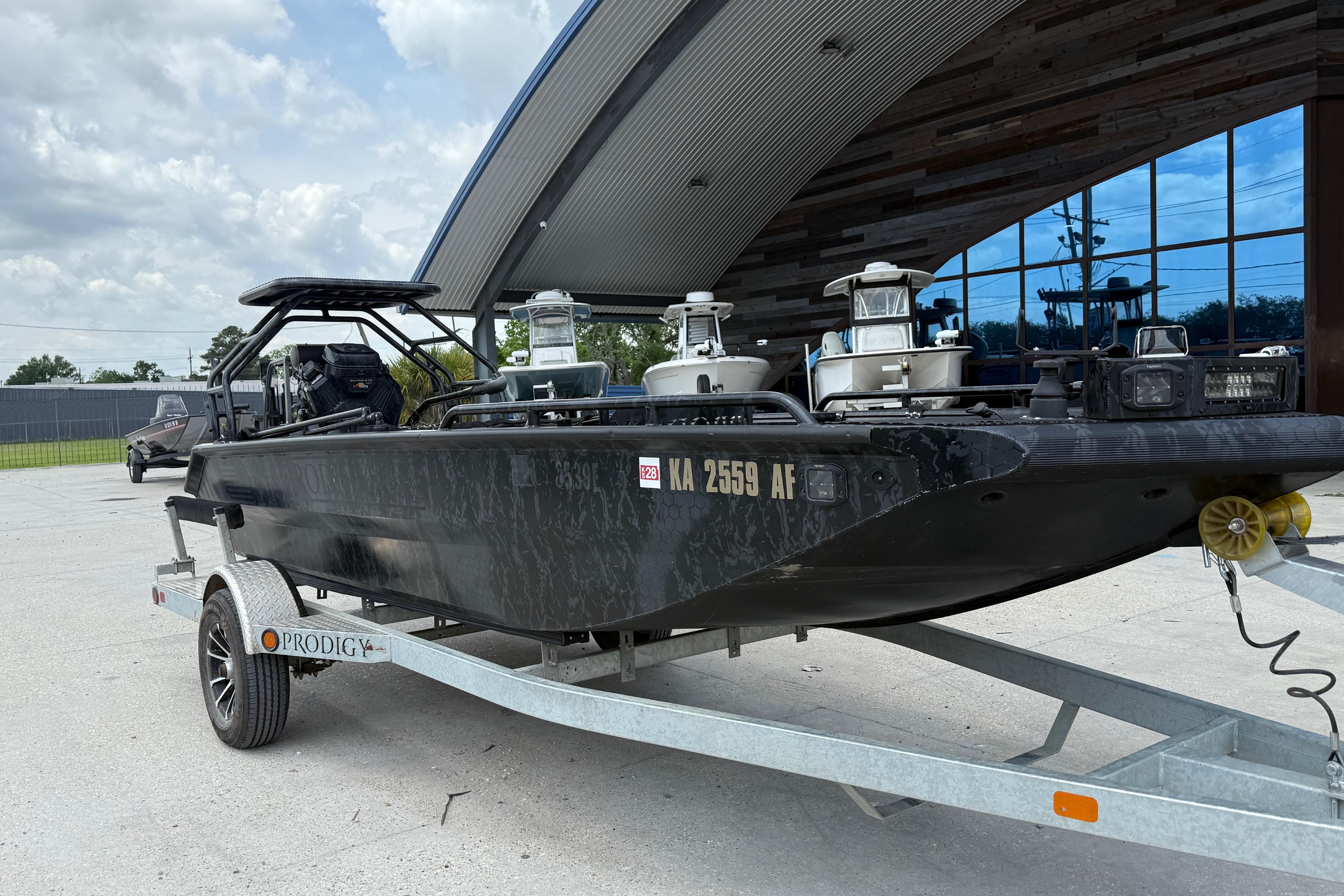 2024 Prodigy 17 boat on trailer, parked outside modern building under cloudy sky.