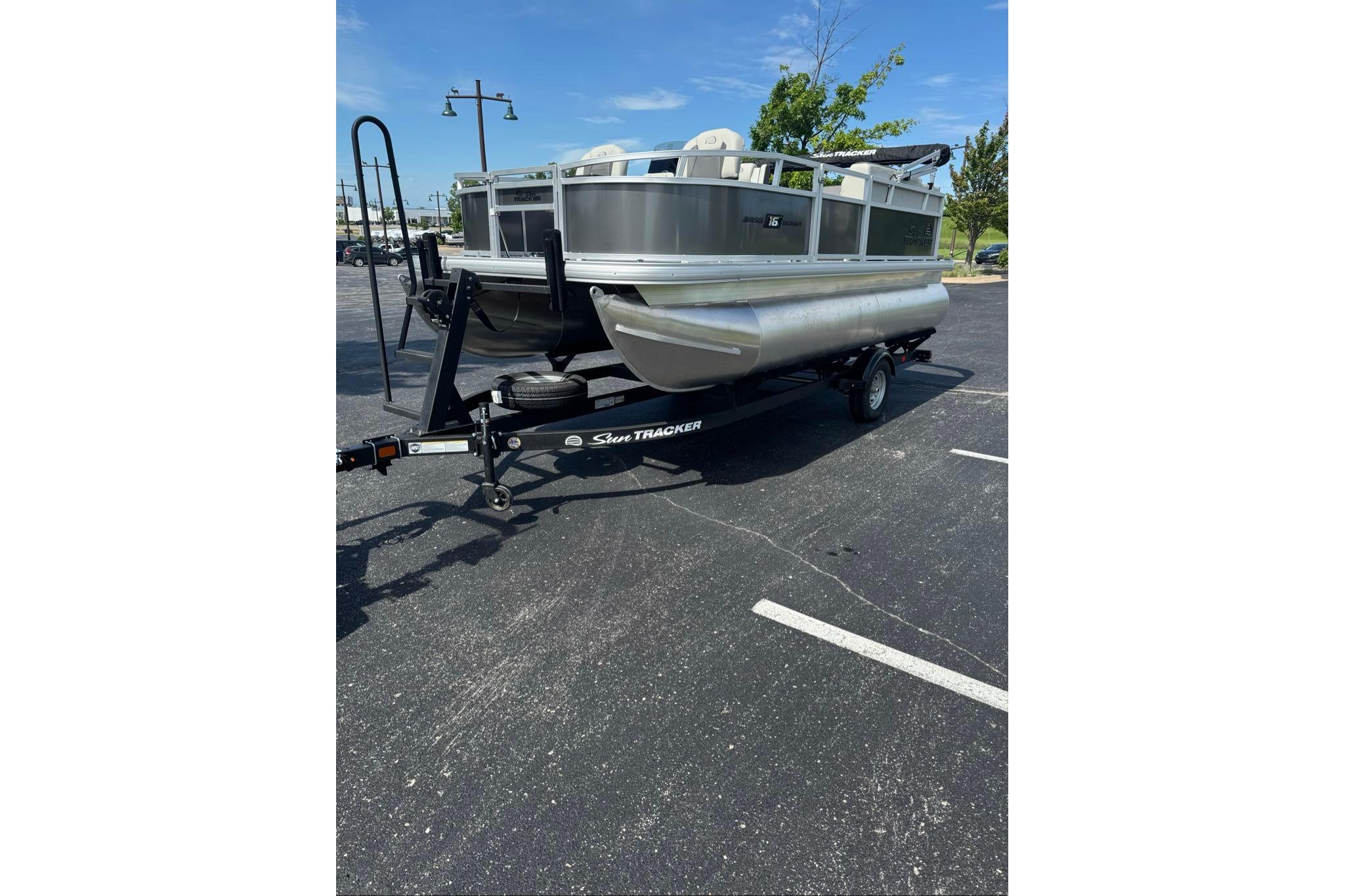 2026 Sun Tracker Bass Buggy 16 XL Select pontoon boat on trailer in parking lot.