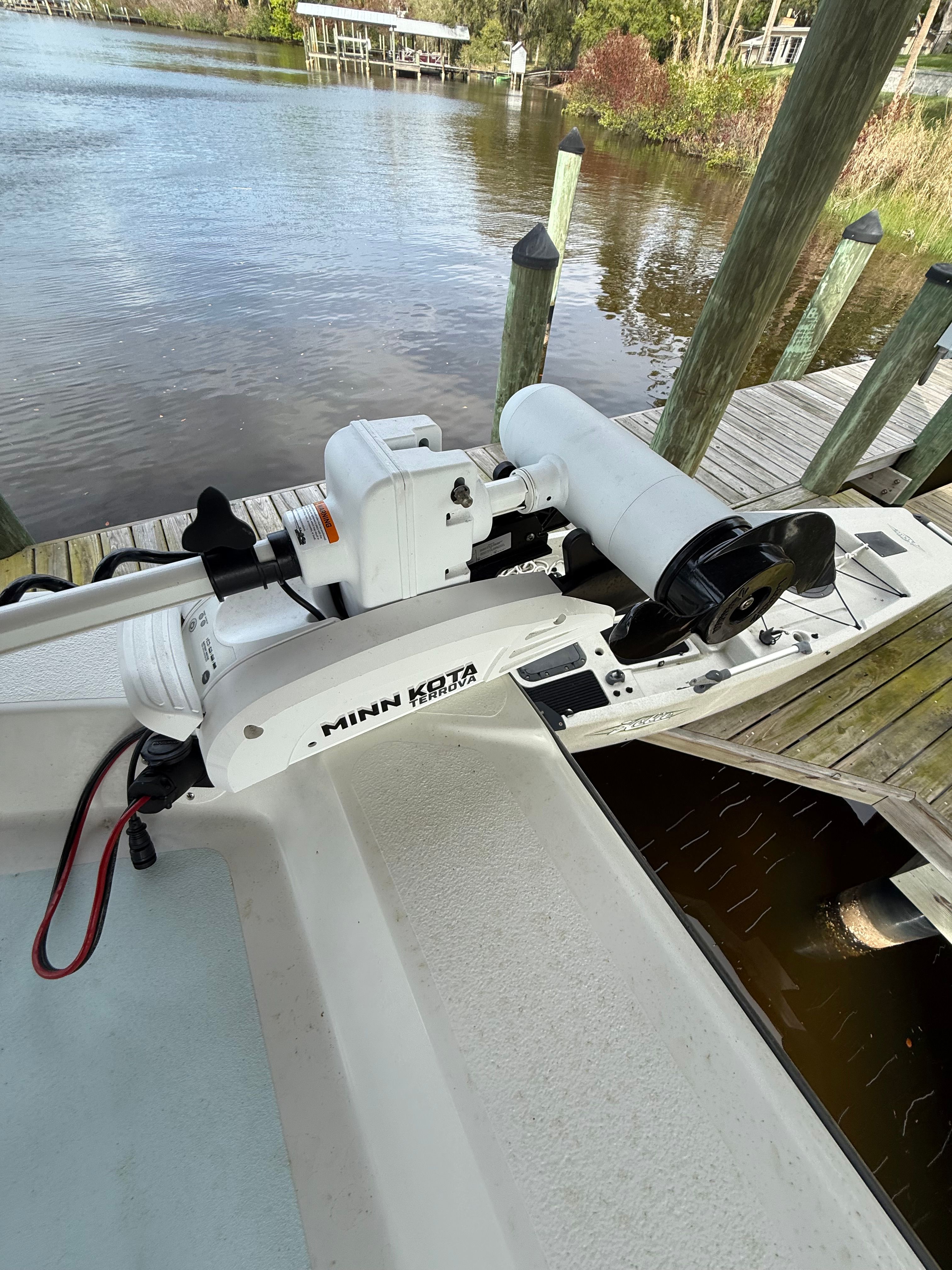 A boat with a Minn Kota motor is docked at a wooden pier on calm water.