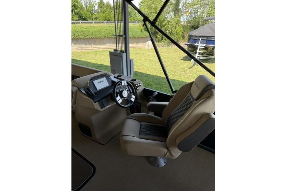Captain's seat and helm of 2025 Harris Sunliner 230 boat, featuring modern controls and steering.