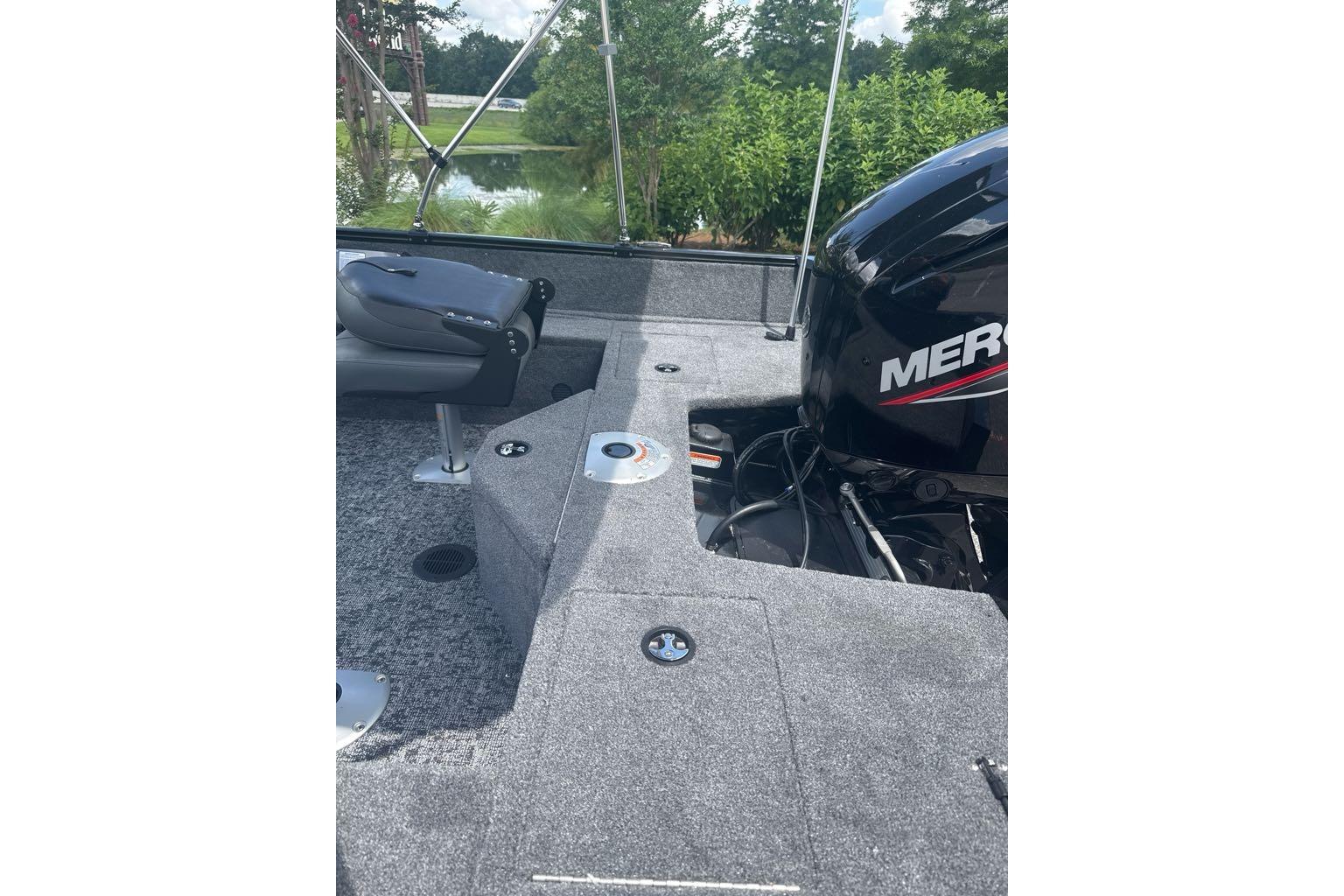 2026 Tracker Pro Guide V-16 SC boat interior with Mercury engine, gray seating, and lush greenery backdrop.