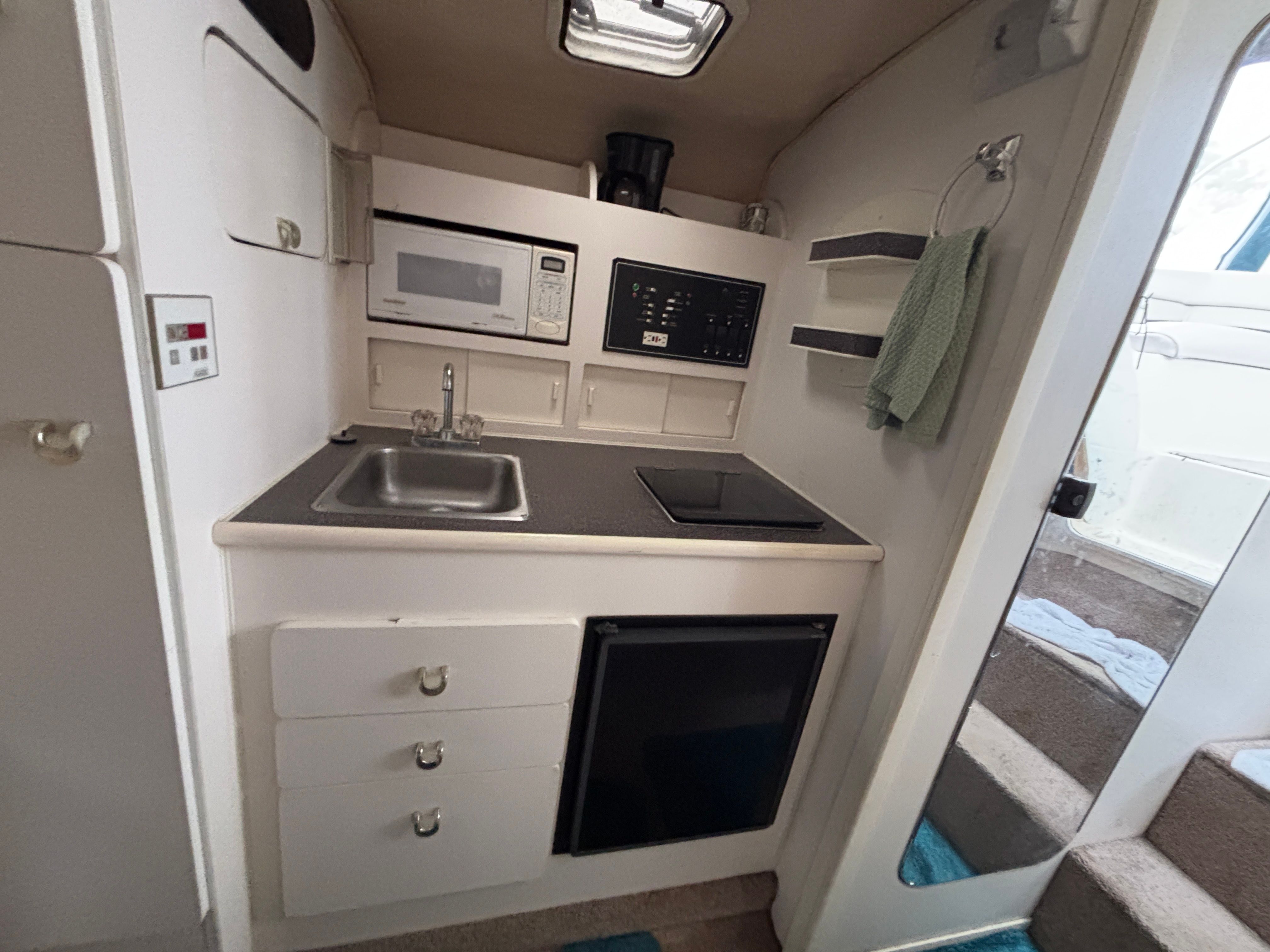 Compact boat kitchen with sink, microwave, and stovetop.