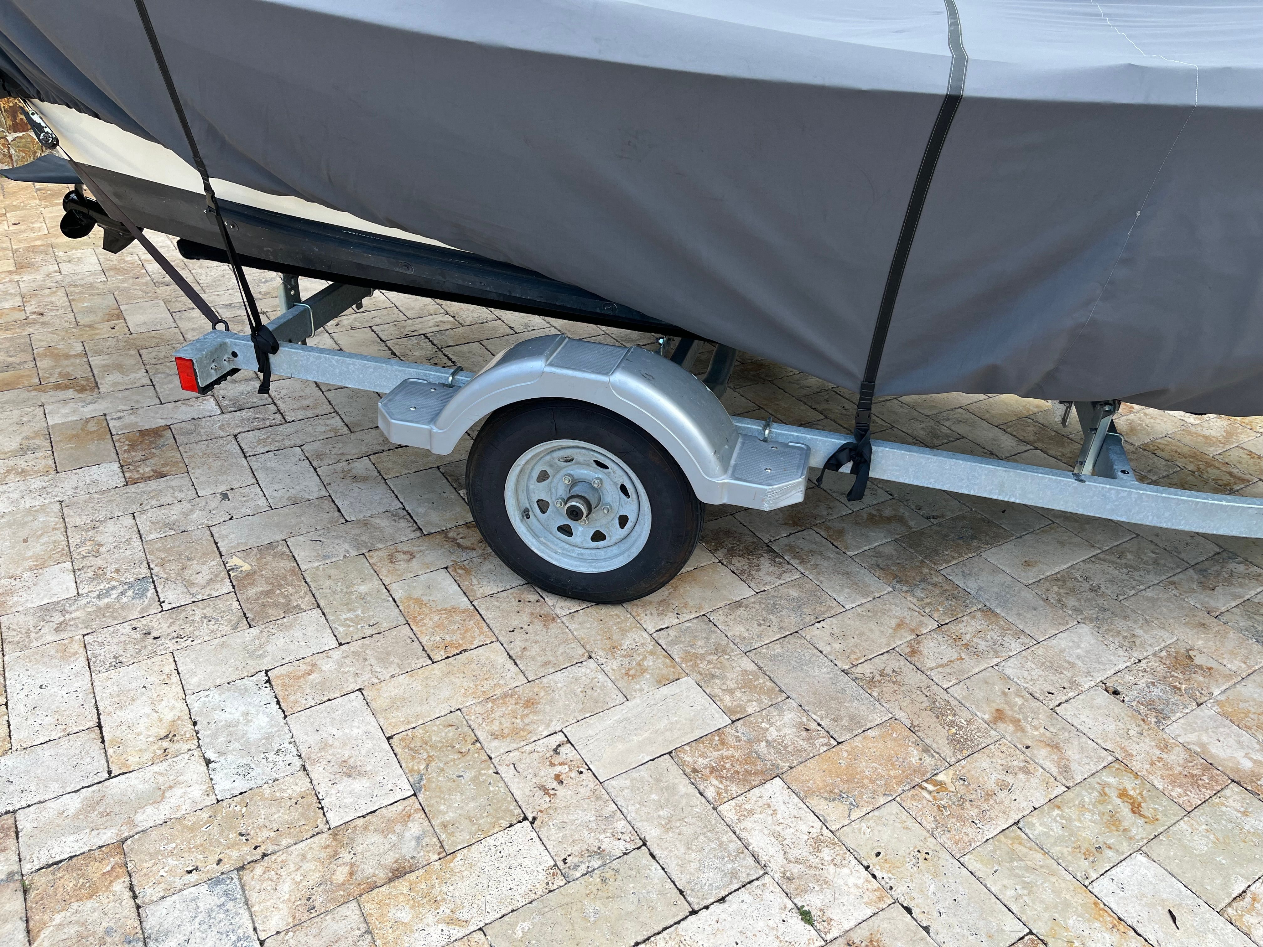 A Dory boat on a trailer, covered with a tarp, sits on a paved surface.