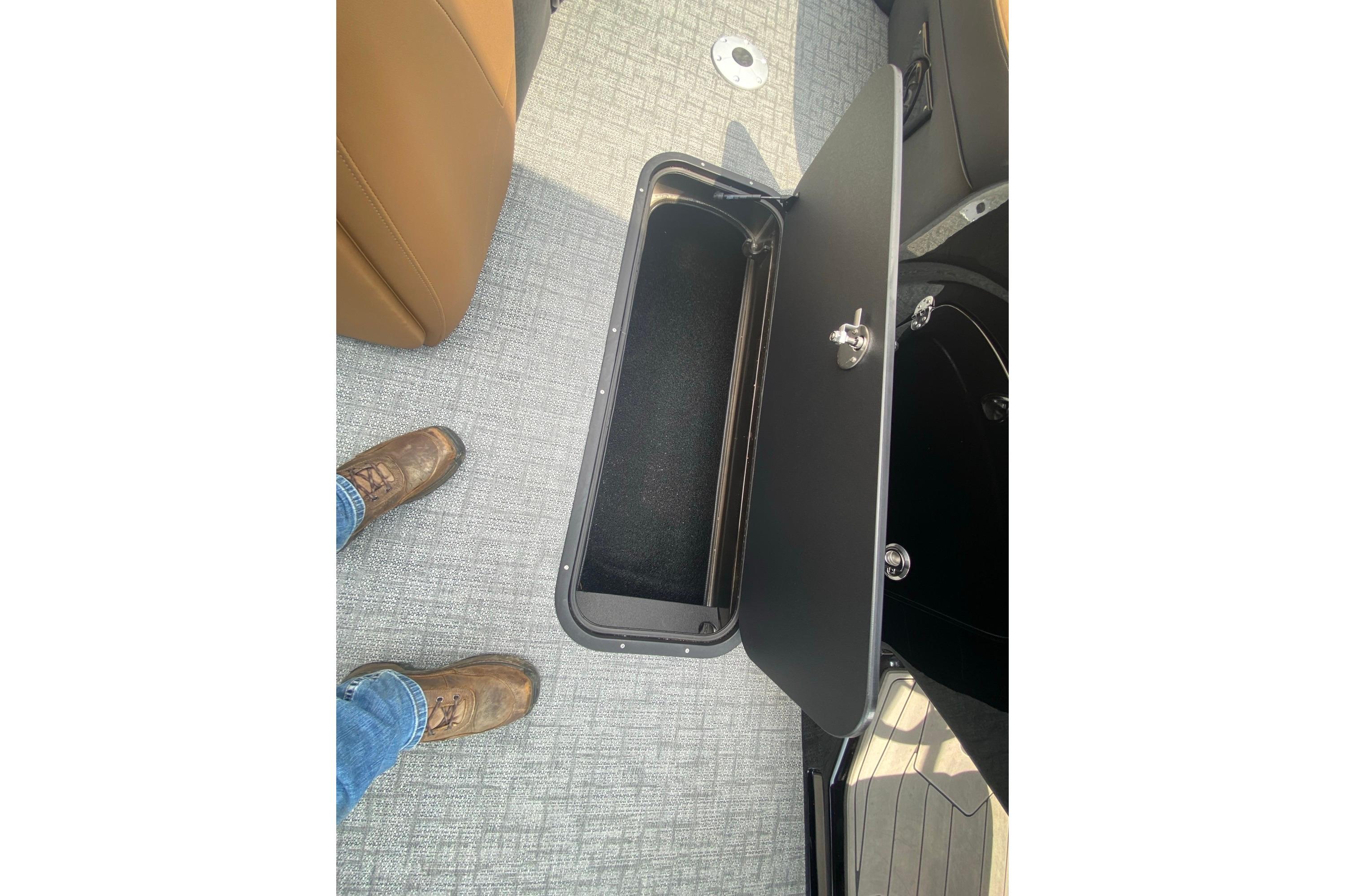 Open storage compartment in 2026 Regency 230 DL boat, with brown seat and gray flooring.