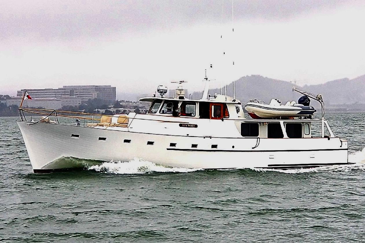 1958 Blanchard Pilothouse yacht cruising on a misty day, with cityscape in background.