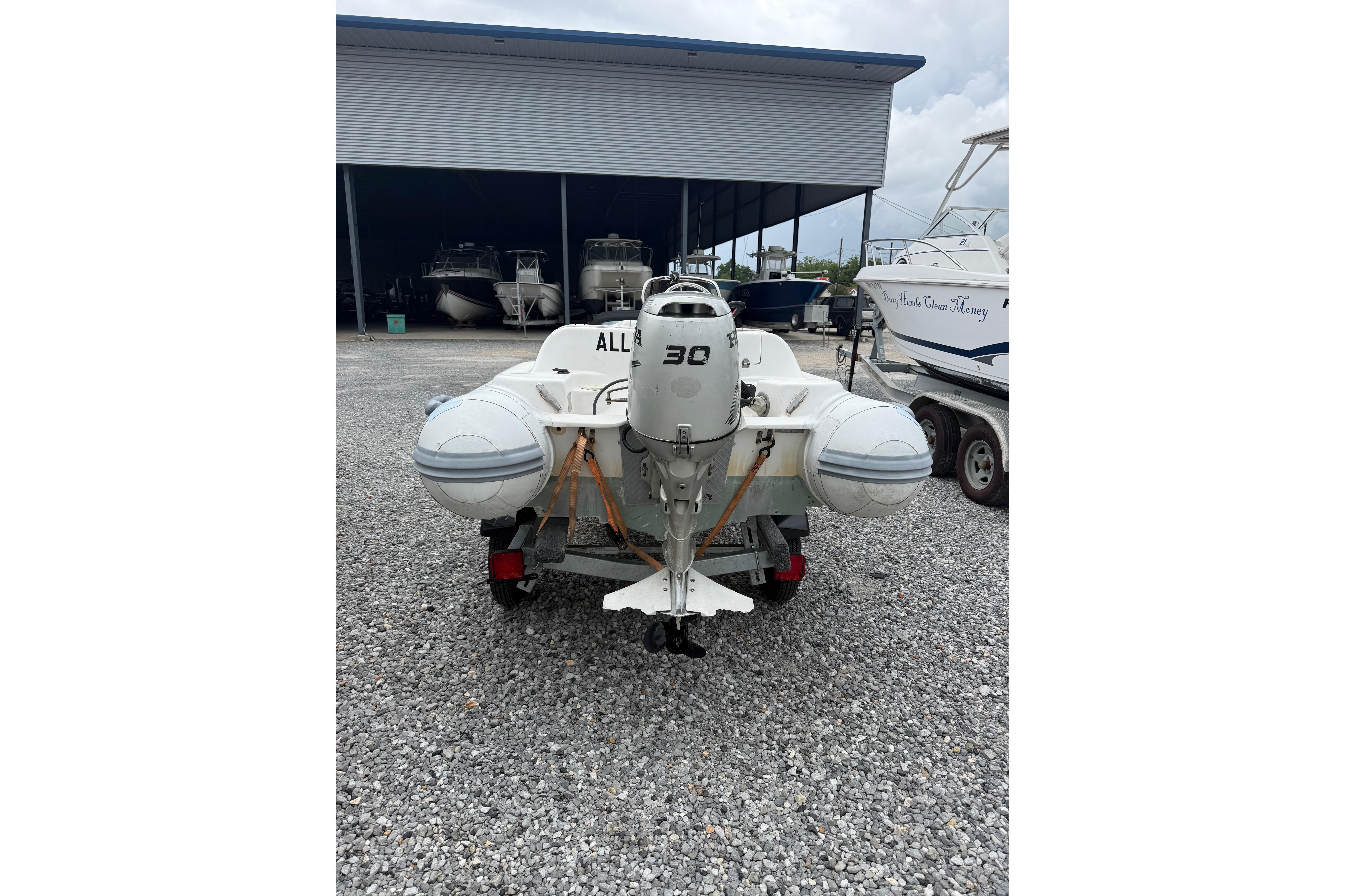 Inflatable boat with 30 HP motor, parked on gravel near boat storage.