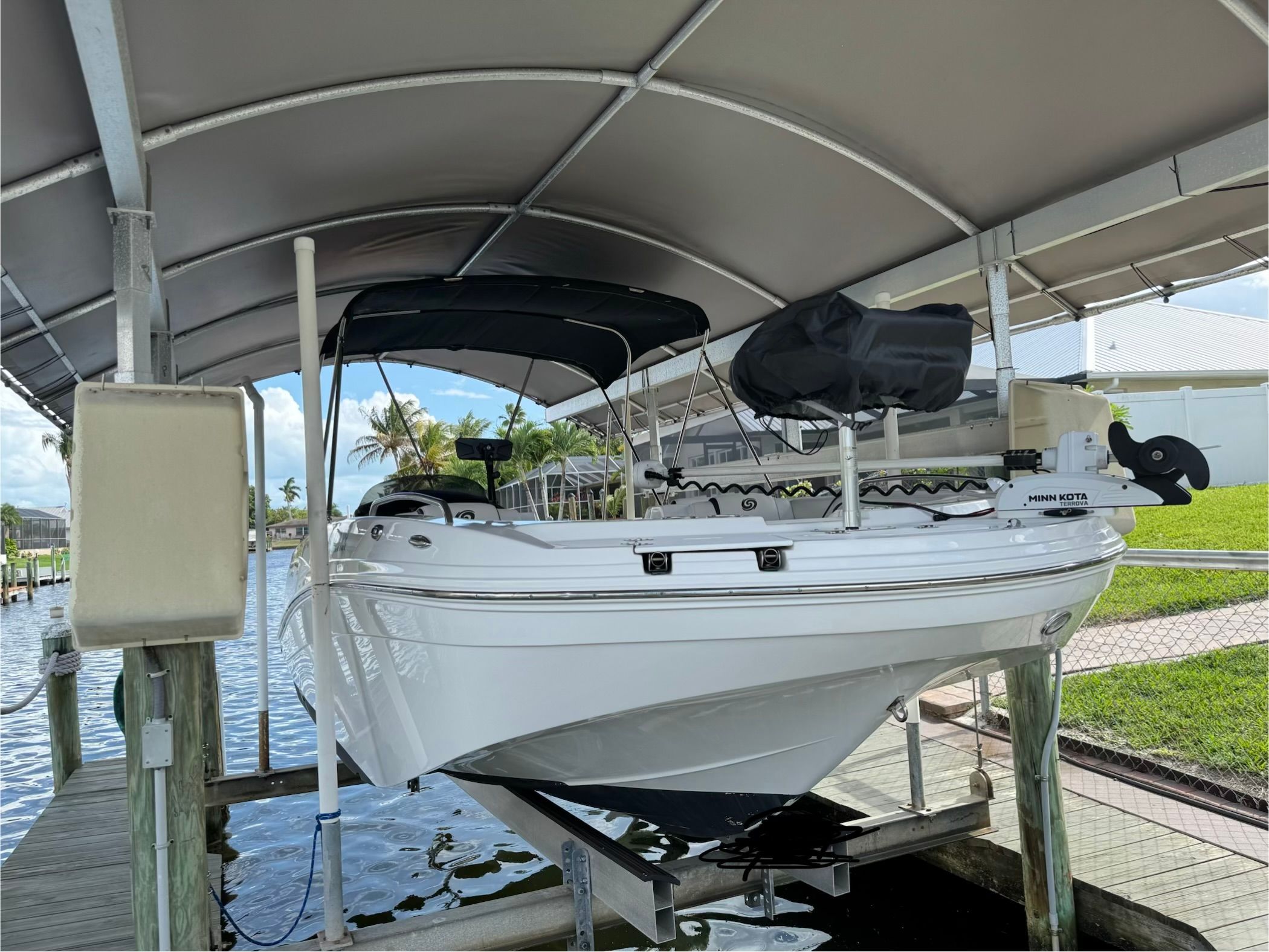 A white boat in a covered dock, featuring a black sunshade.