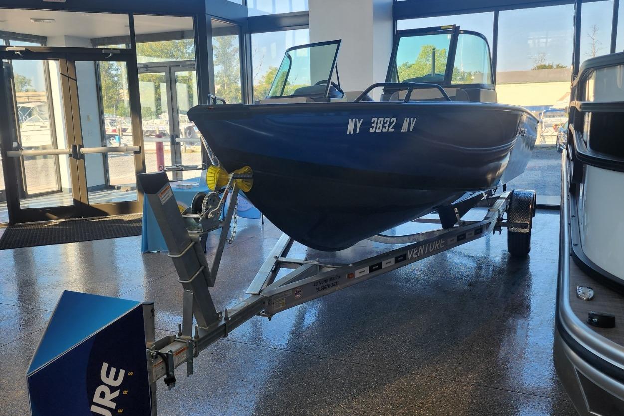 2023 Lowe boat on trailer inside showroom, featuring blue hull and glass windows.