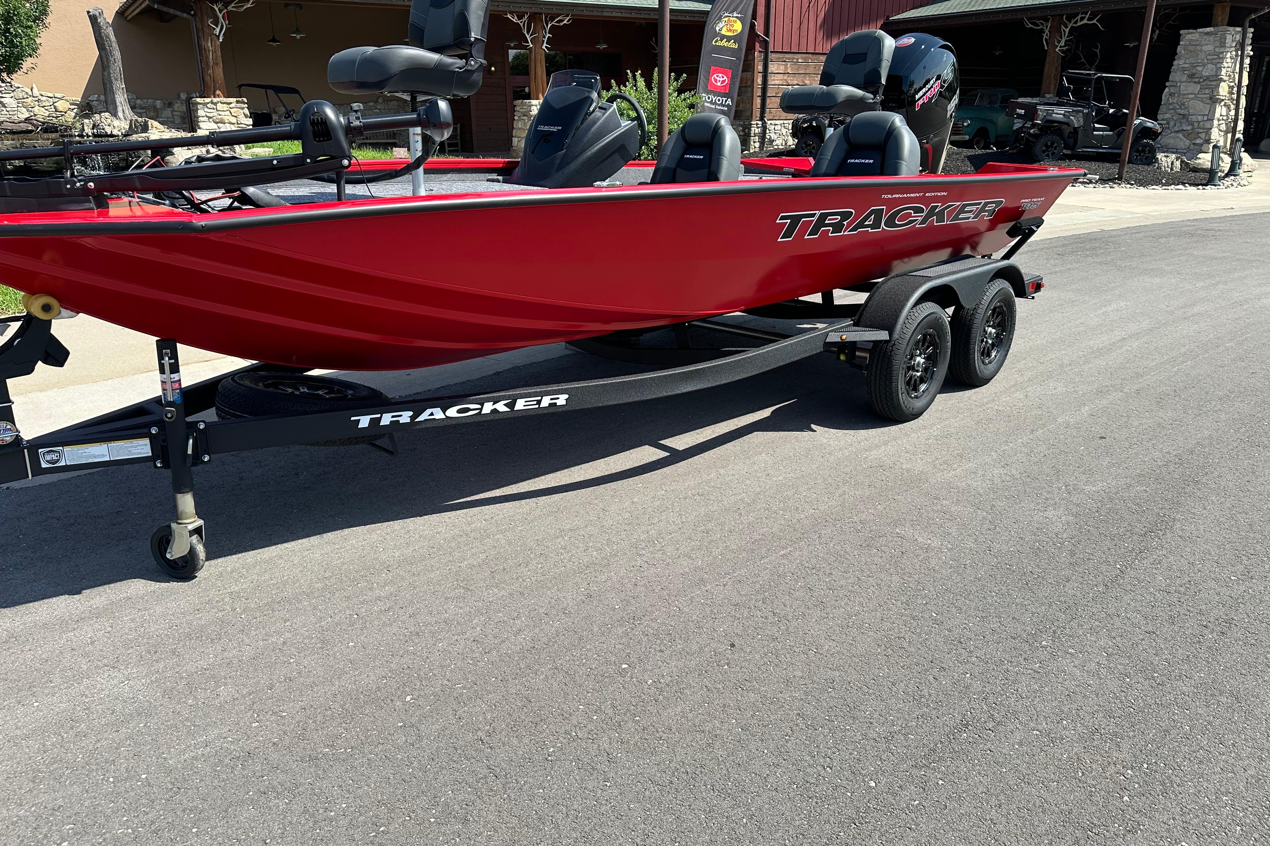 Red 2026 Tracker Pro Team 195 boat on trailer, parked on a paved road.