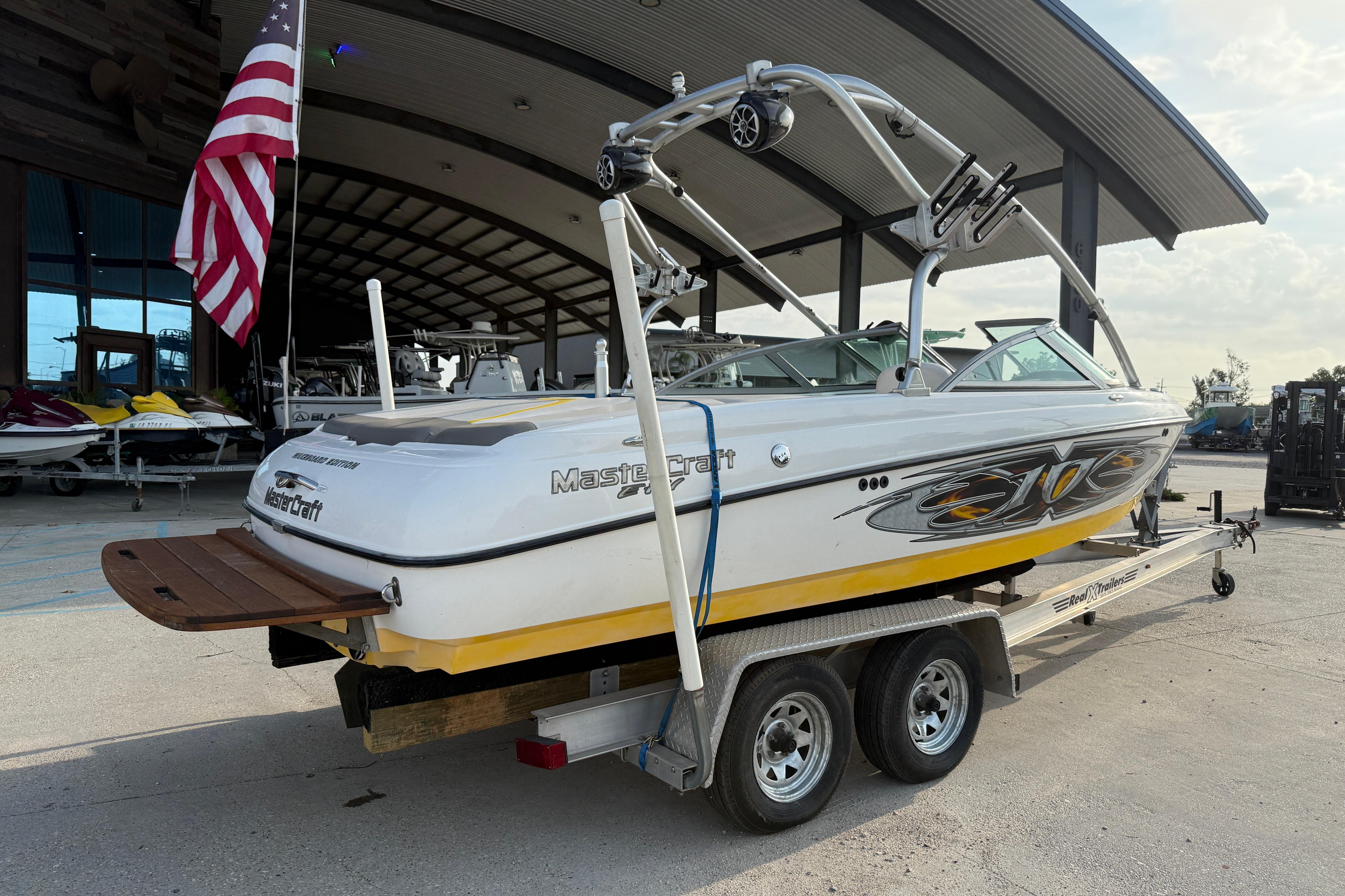 2005 MasterCraft X10 boat on trailer, parked near a building with an American flag.