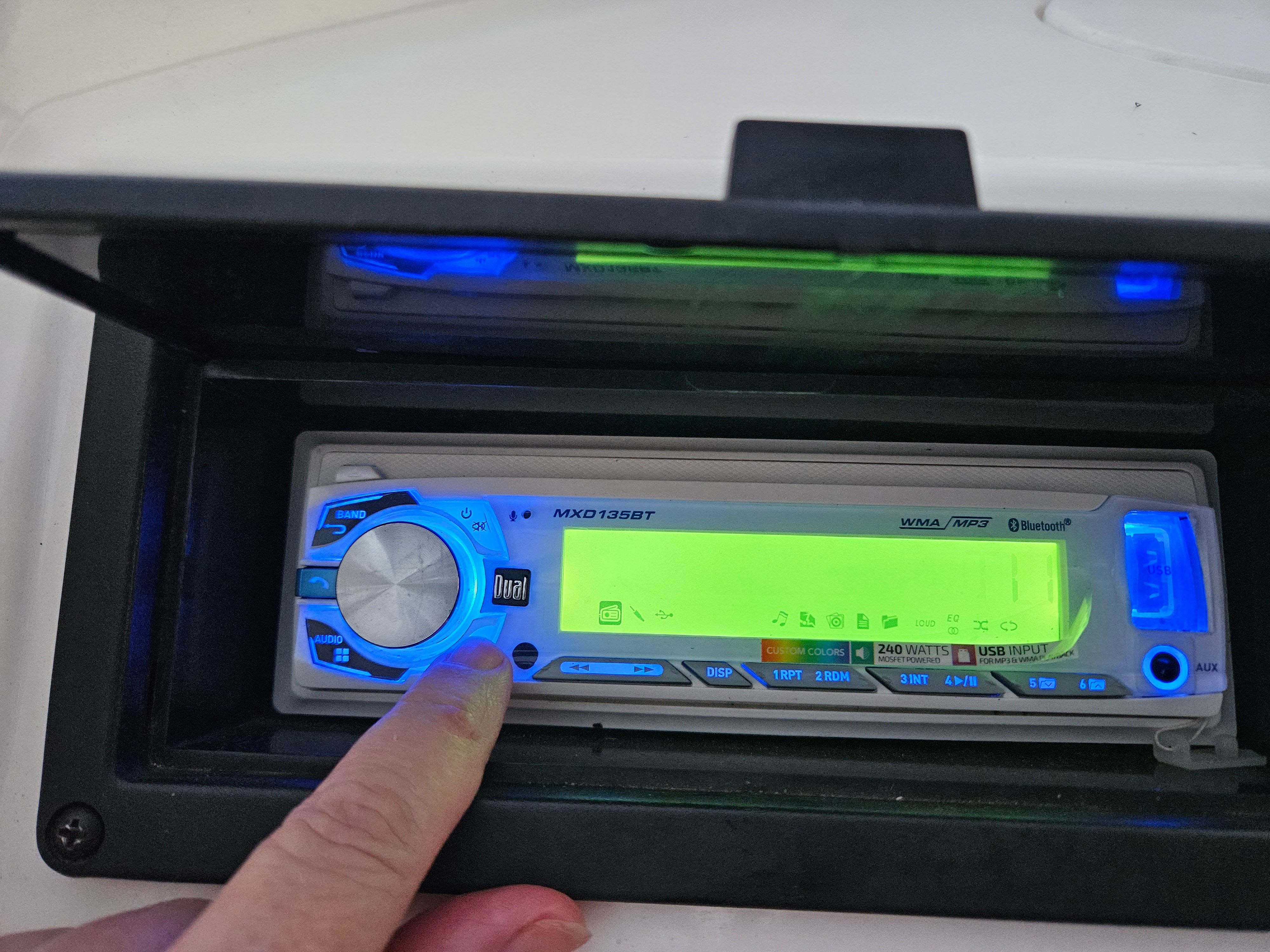 A finger points to a blue-lit car stereo in a boat.