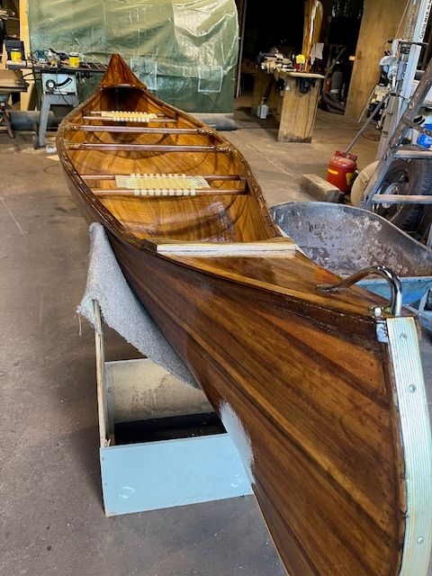 A handcrafted cedar strip canoe is in a workshop.