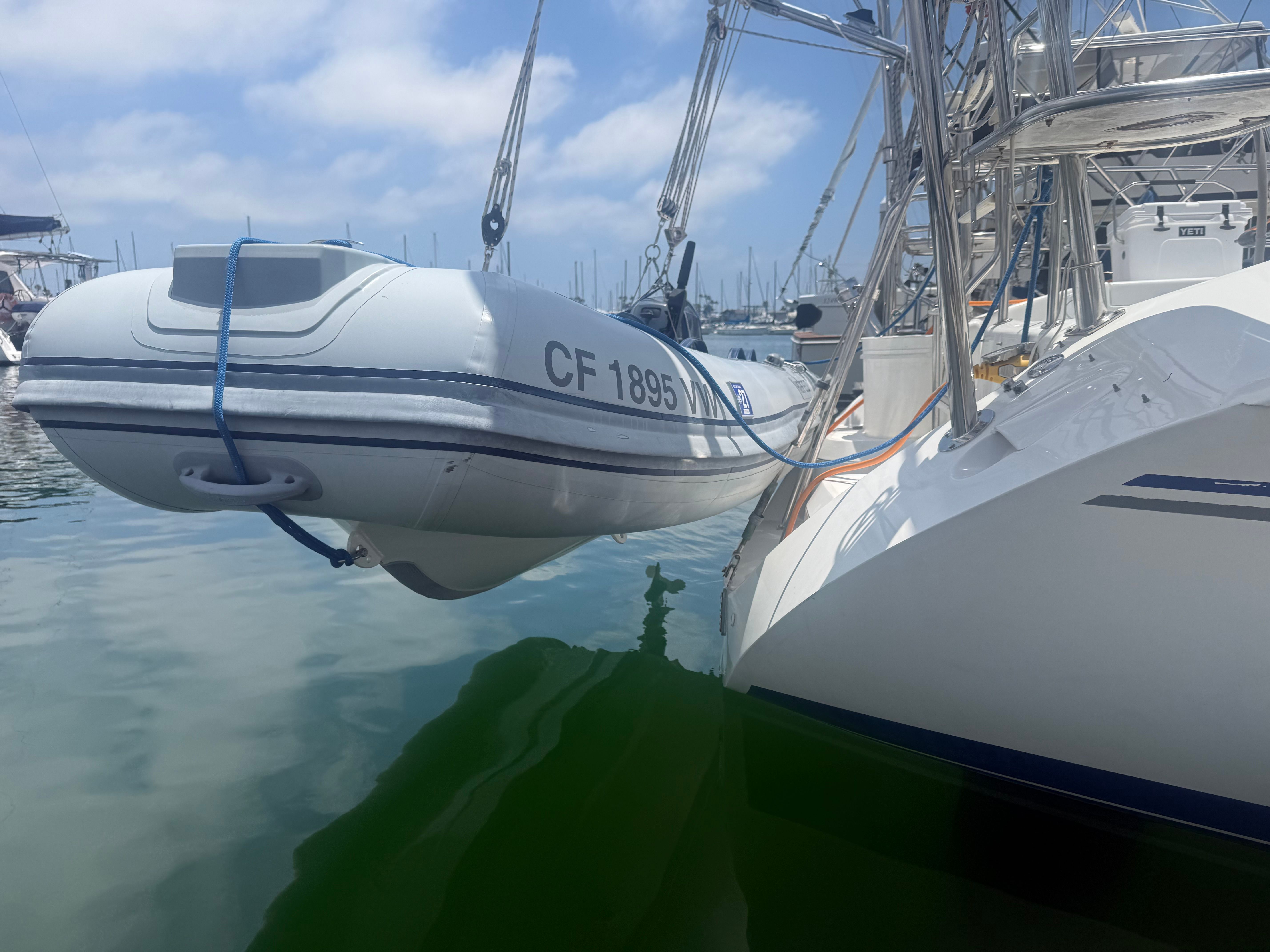 A white inflatable boat is suspended alongside a larger boat in the harbor.