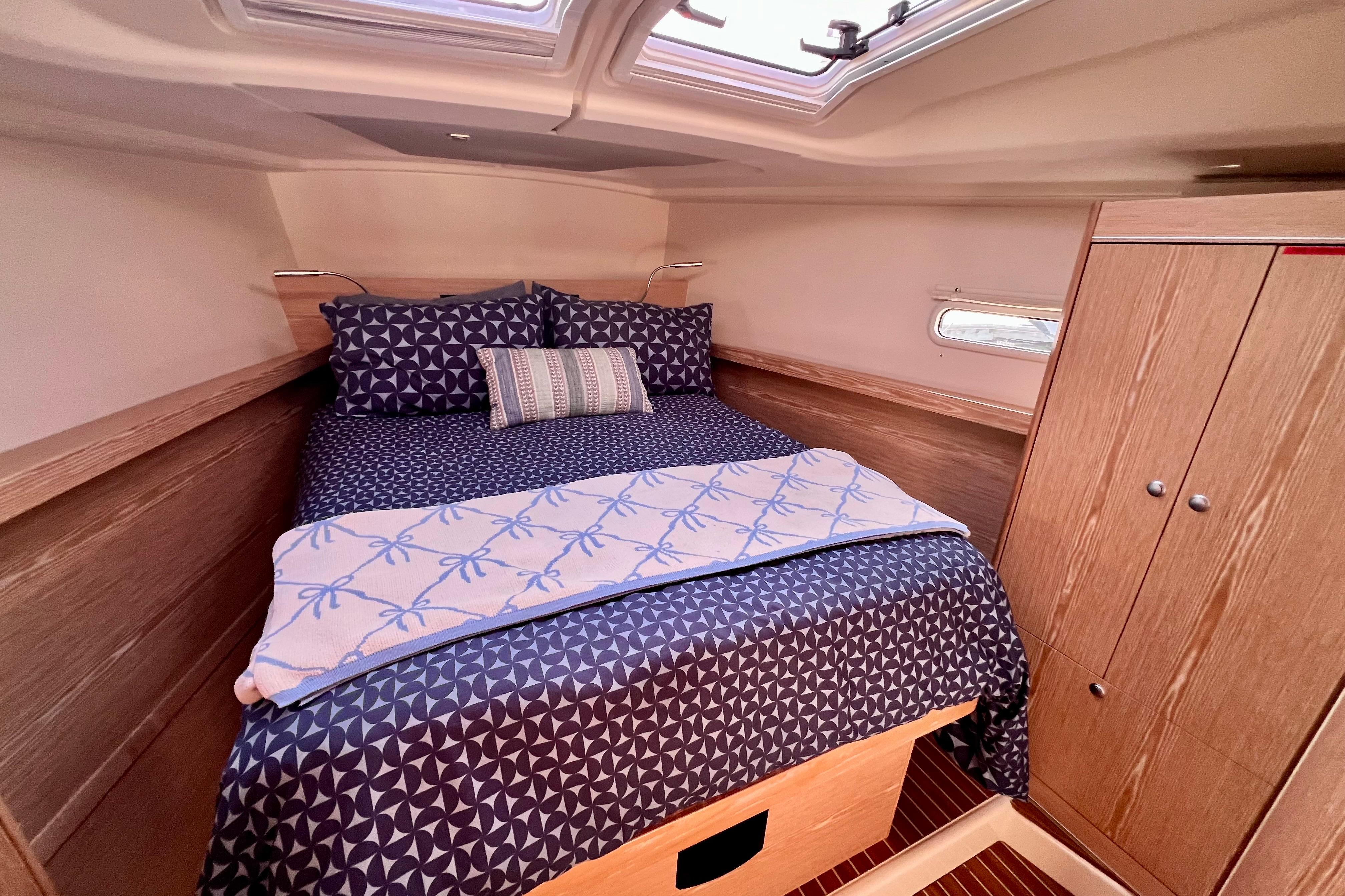 Cozy cabin interior of 2016 Hanse 455 yacht with patterned bedding and wooden cabinetry.