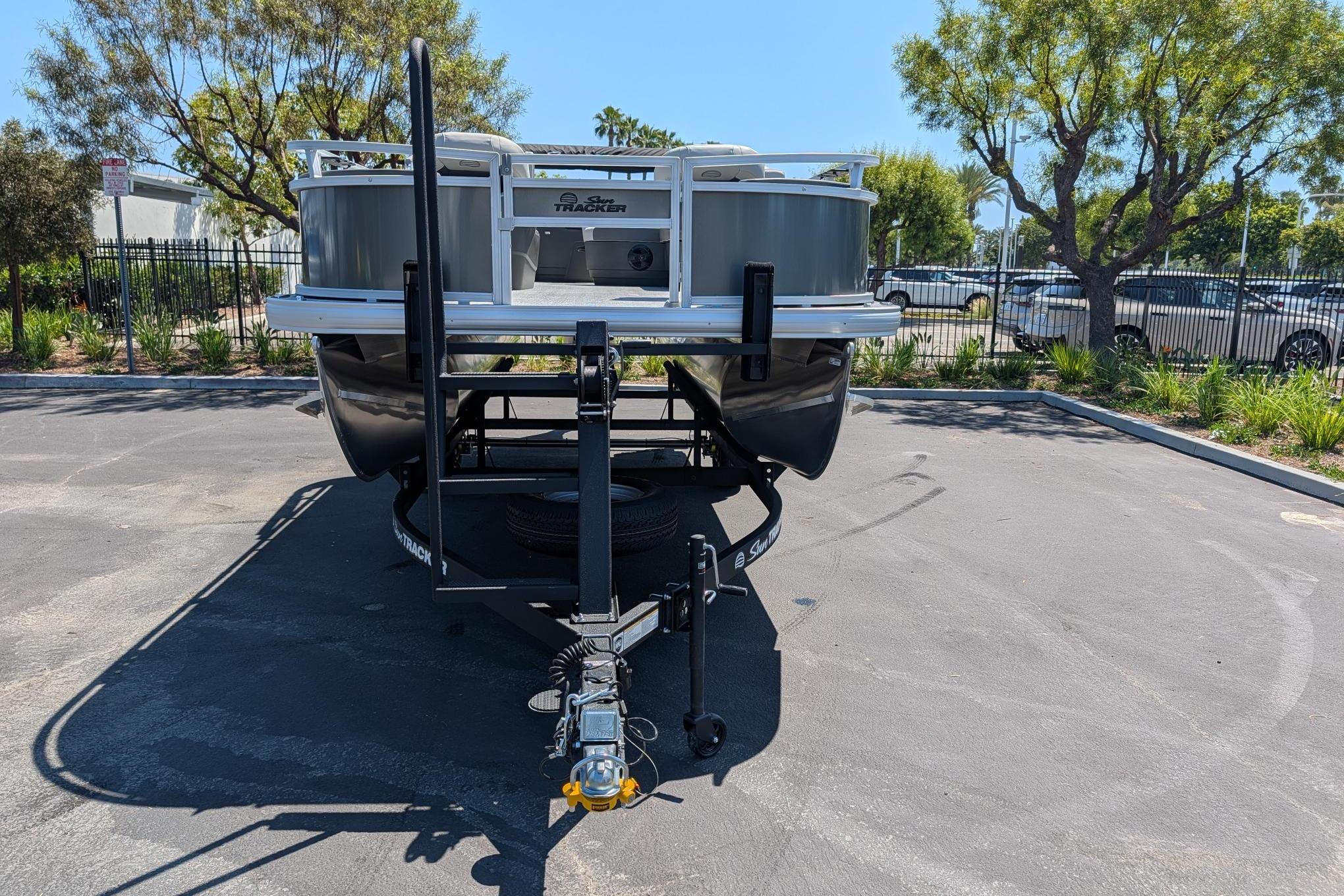 2026 Sun Tracker Bass Buggy 18 DLX pontoon boat on trailer in parking lot.