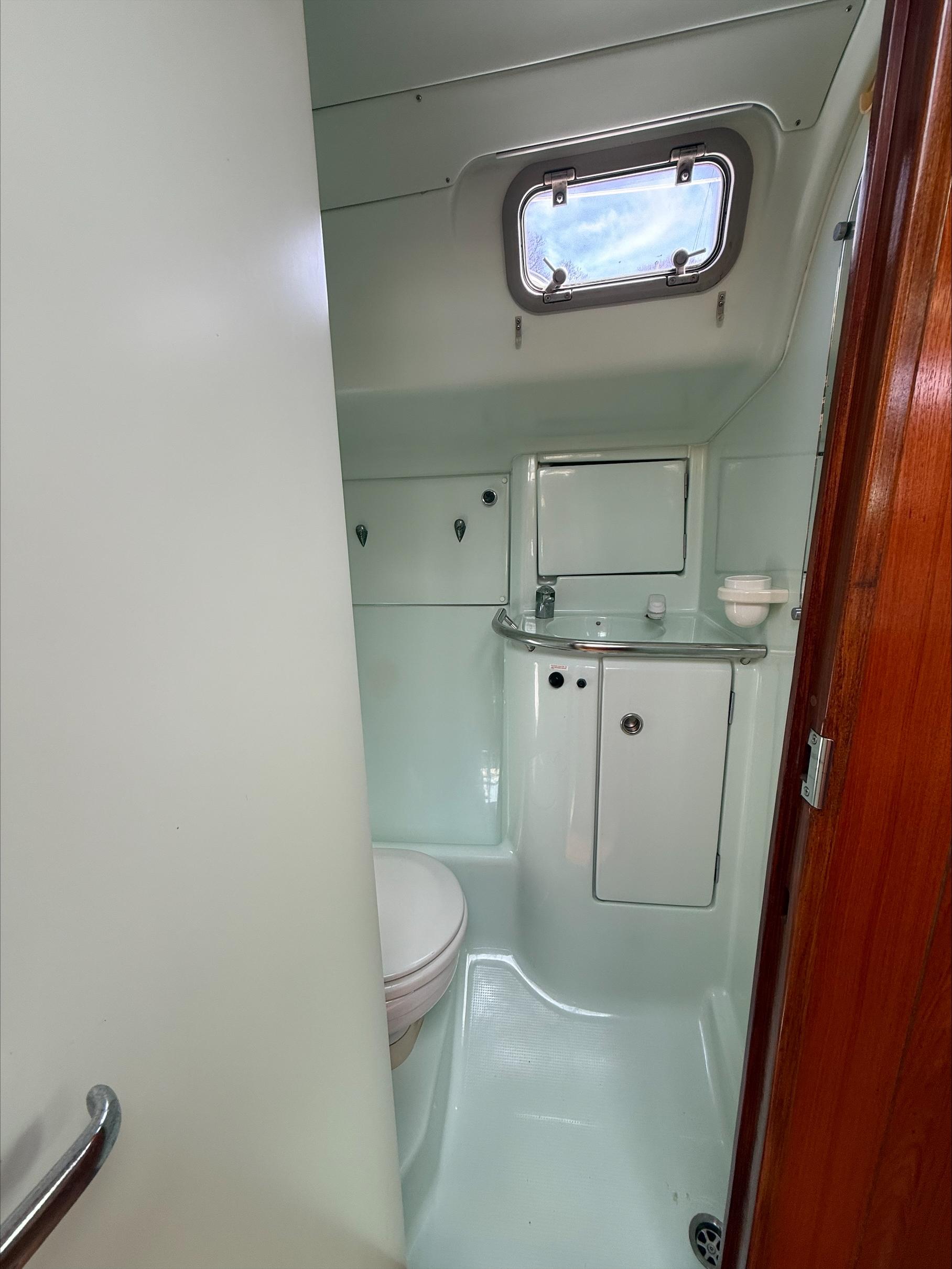 Bathroom interior of 1993 Beneteau Oceanis 400 sailboat, featuring compact design and porthole window.