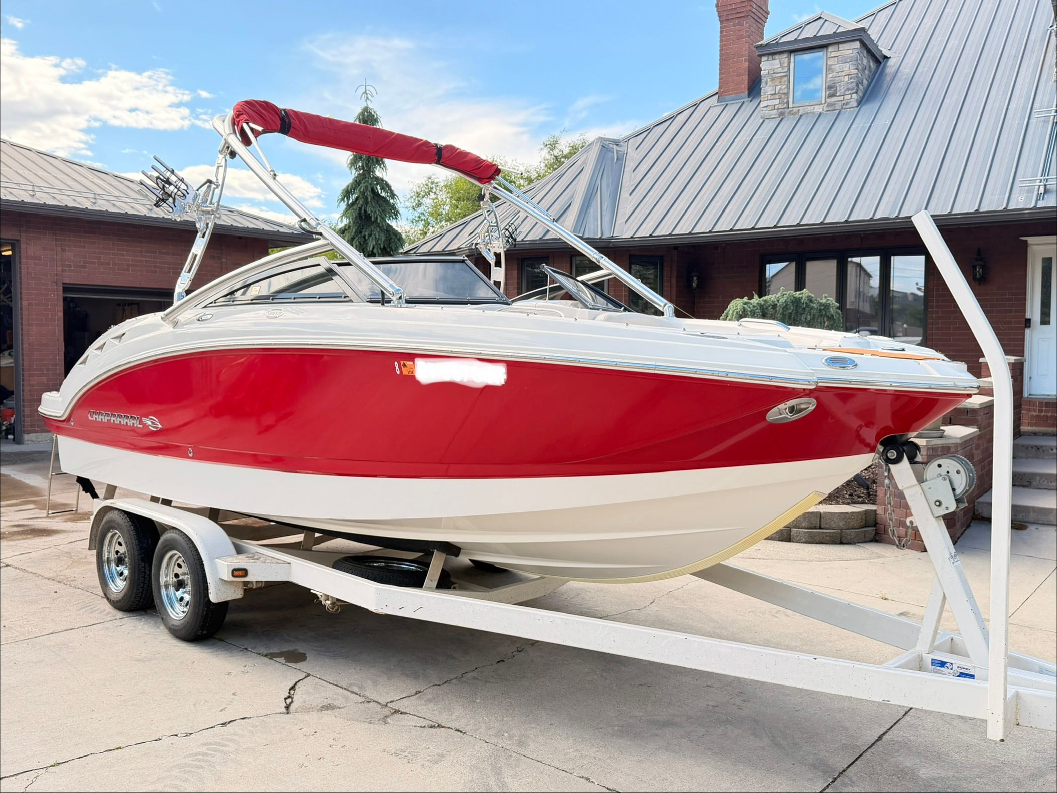 A red 2008 Chaparral Sunesta 224 boat on a trailer in front of a house.