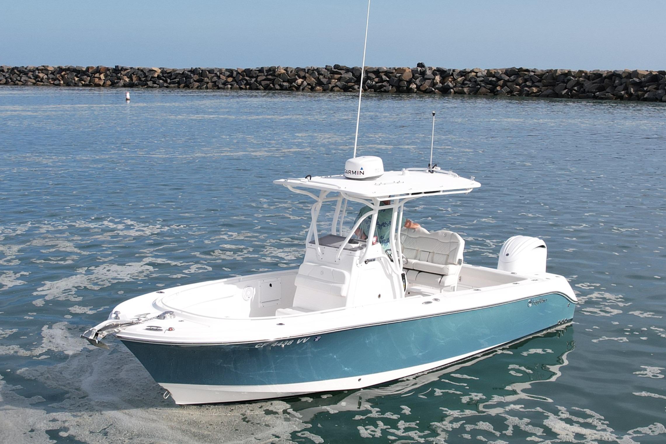 2023 Edgewater 245CC boat on calm water near a rocky shoreline.