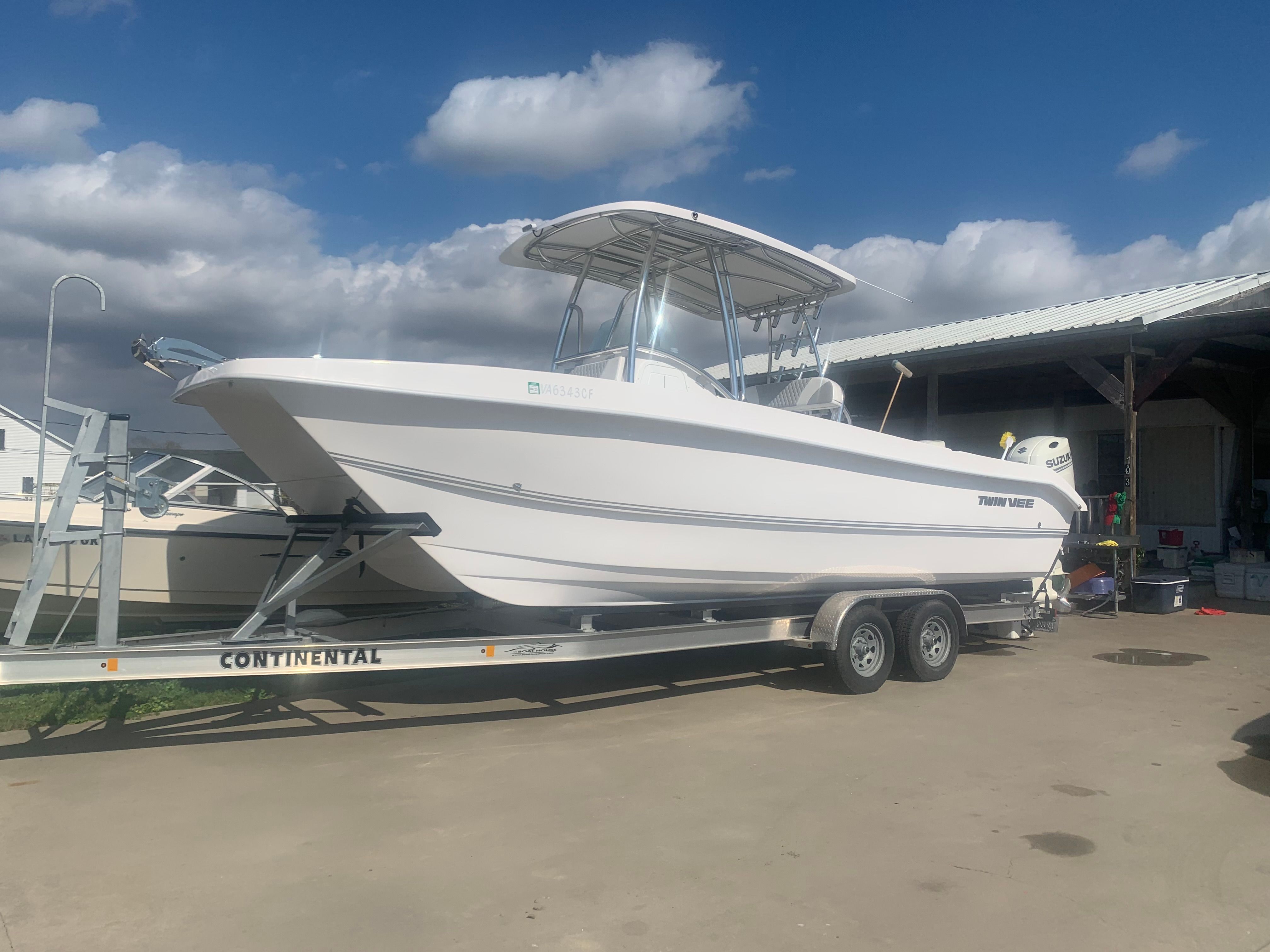 A Twin Vee Ocean Cat boat on a trailer, parked on concrete under a cloudy sky.