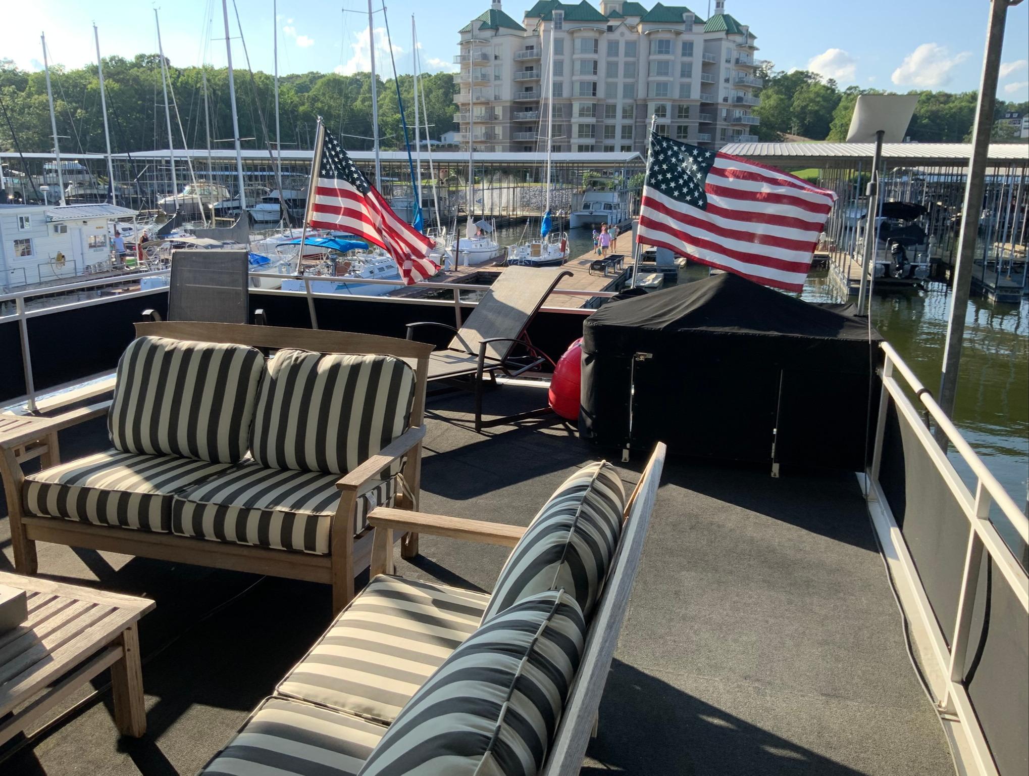 2007 Skipperliner 640 houseboat deck with striped seating and American flags at marina.