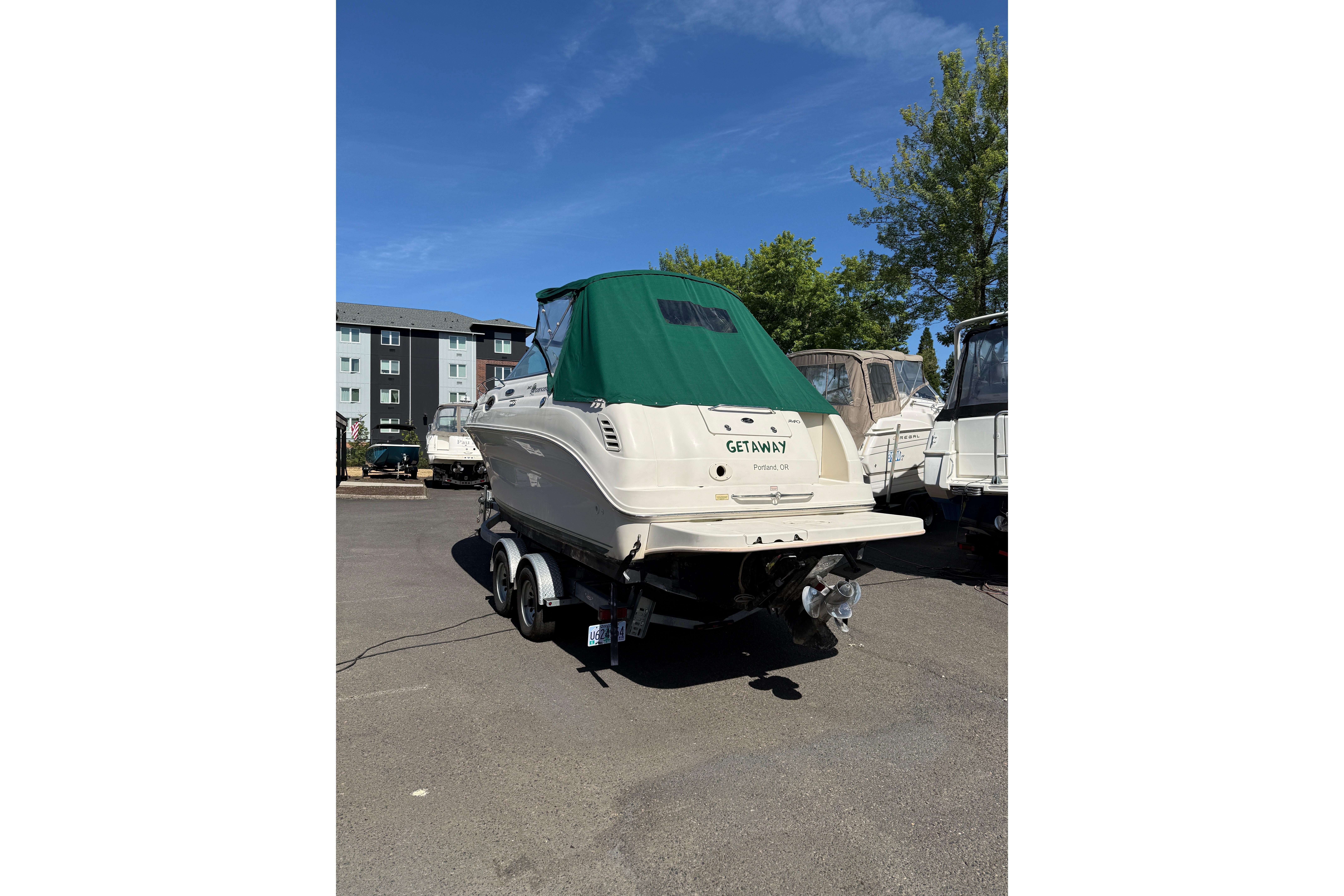 2004 Sea Ray 240 Sundancer boat with green cover on trailer in parking lot.