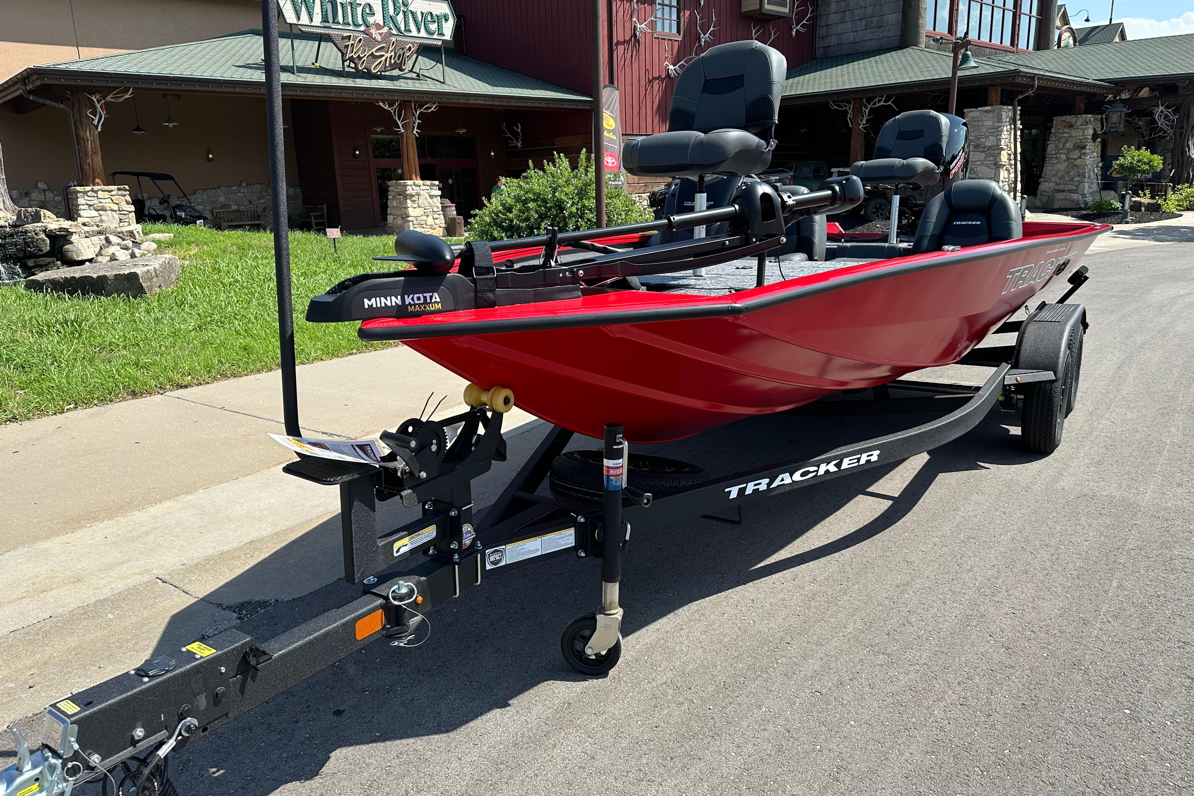 2026 Tracker Pro Team 195 boat in red on a trailer, parked outside a shop.