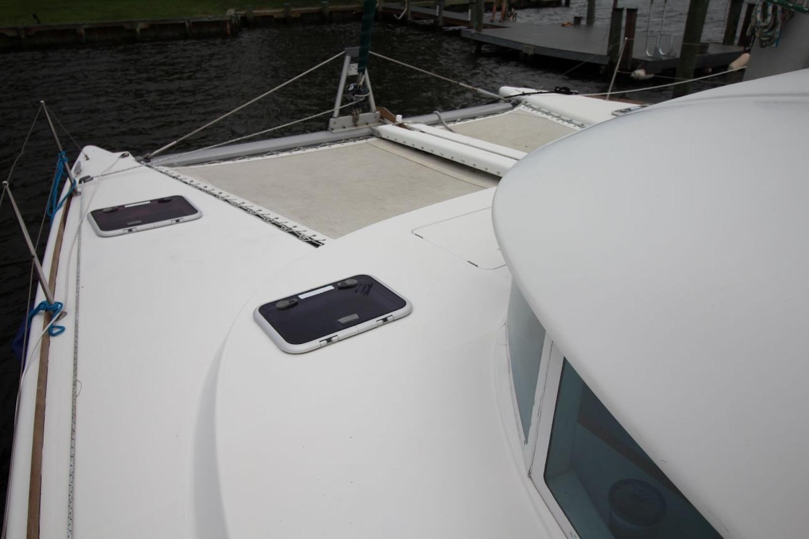 2004 Lagoon 380 catamaran deck with hatches and netting, docked by the water.
