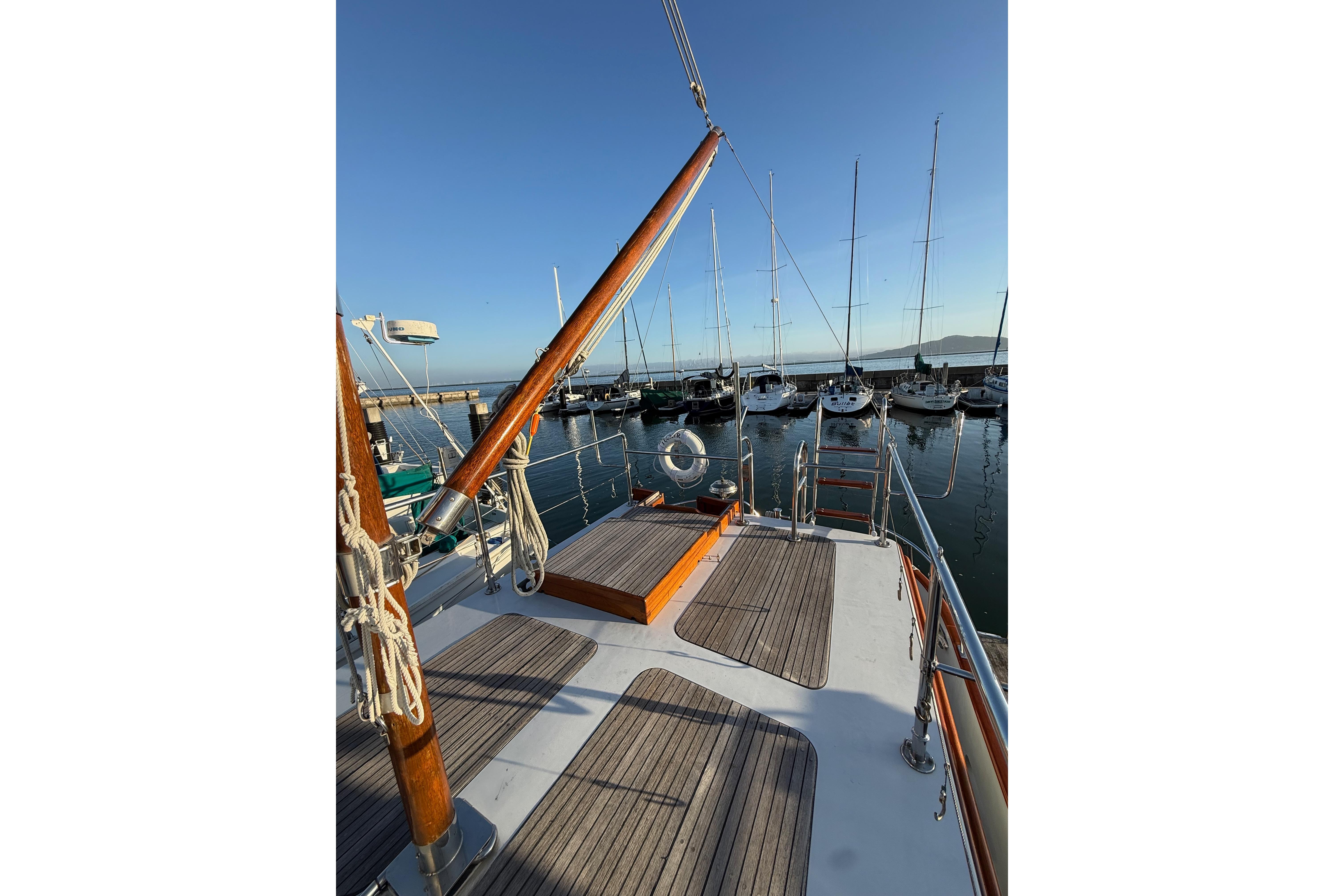 1987 Lord Nelson Victory Tug docked at marina, wooden deck, clear sky, sailboats in background.