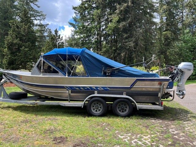 1986 Custom Jet Boat with blue cover on trailer in forest setting.