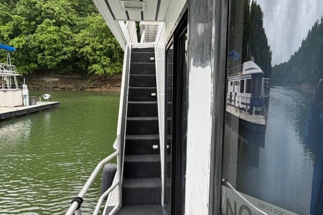 1997 Stardust Houseboat 18x83 with exterior stairs, docked on a serene lake.