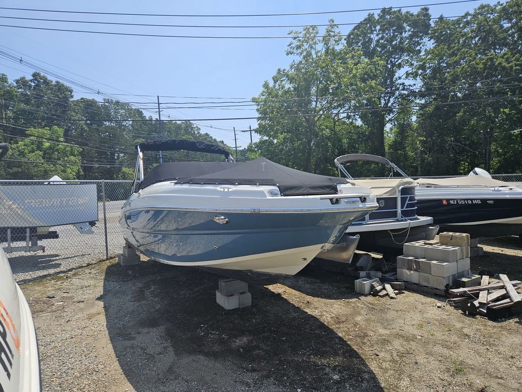 A Stingray 231 DC boat is on dry land, surrounded by trees and other boats.