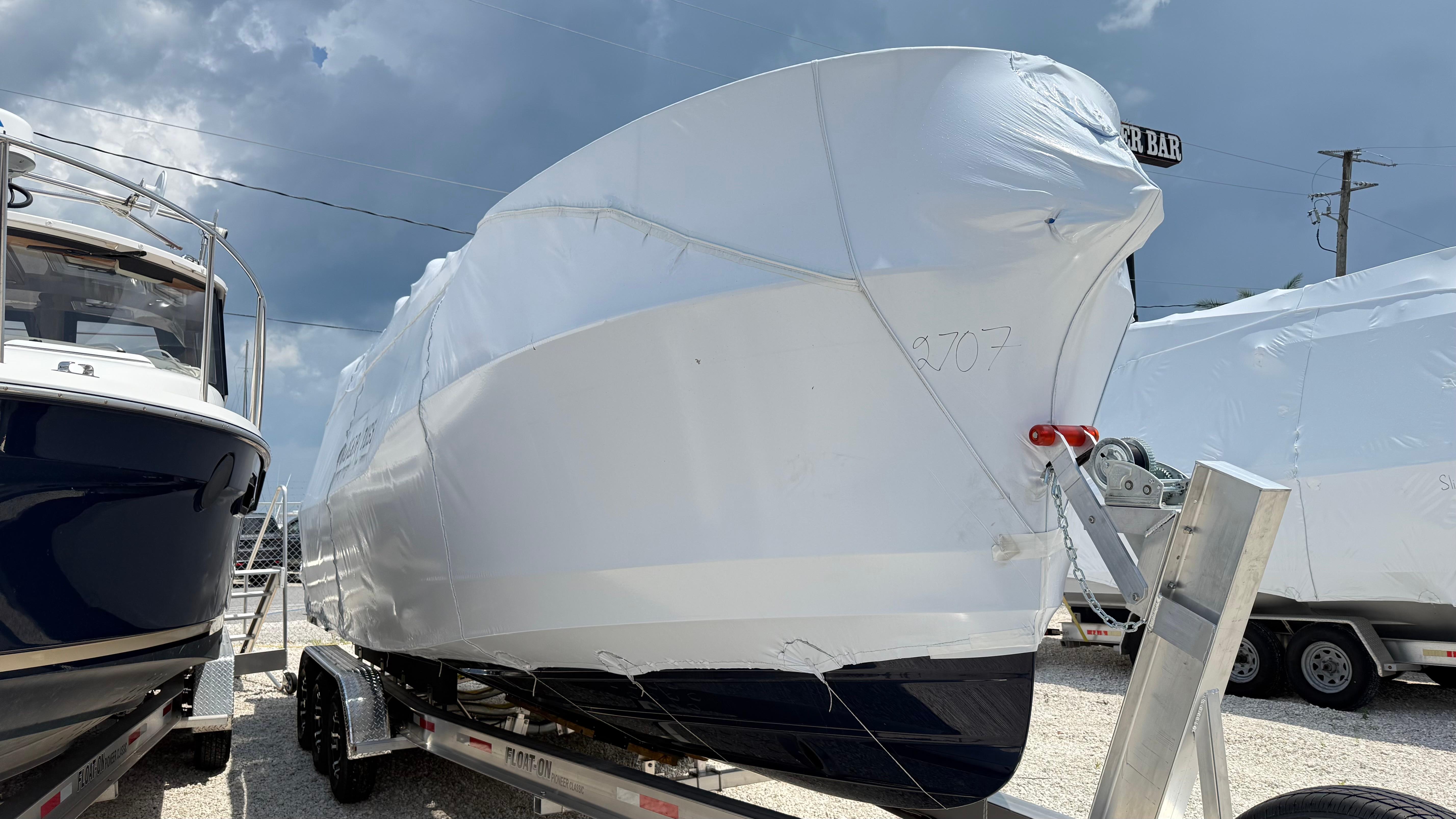 2026 Ranger Tugs R-27 boat covered in protective wrap on a trailer under cloudy skies.