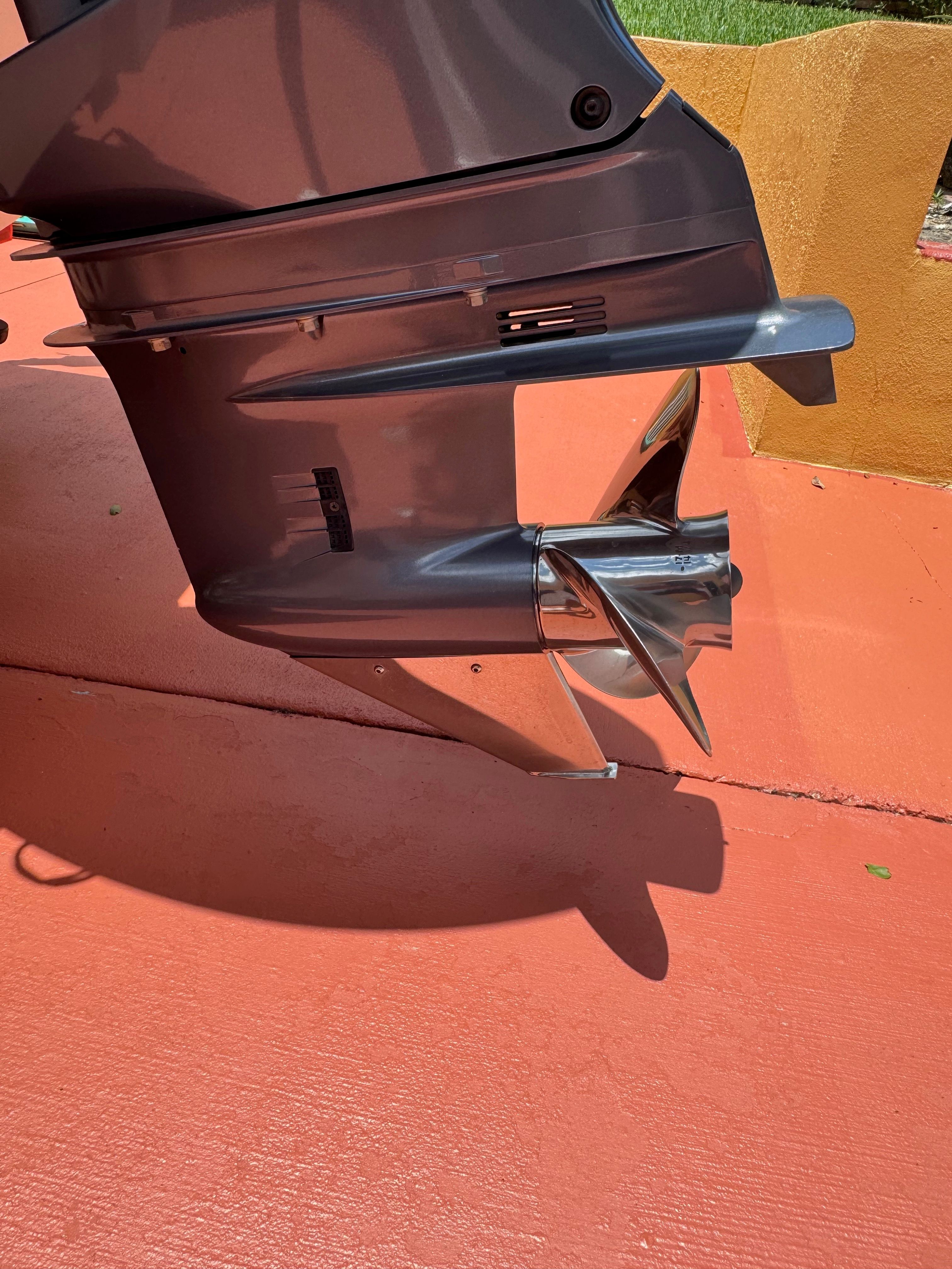 Close-up of a shiny outboard motor with propeller on an orange surface.