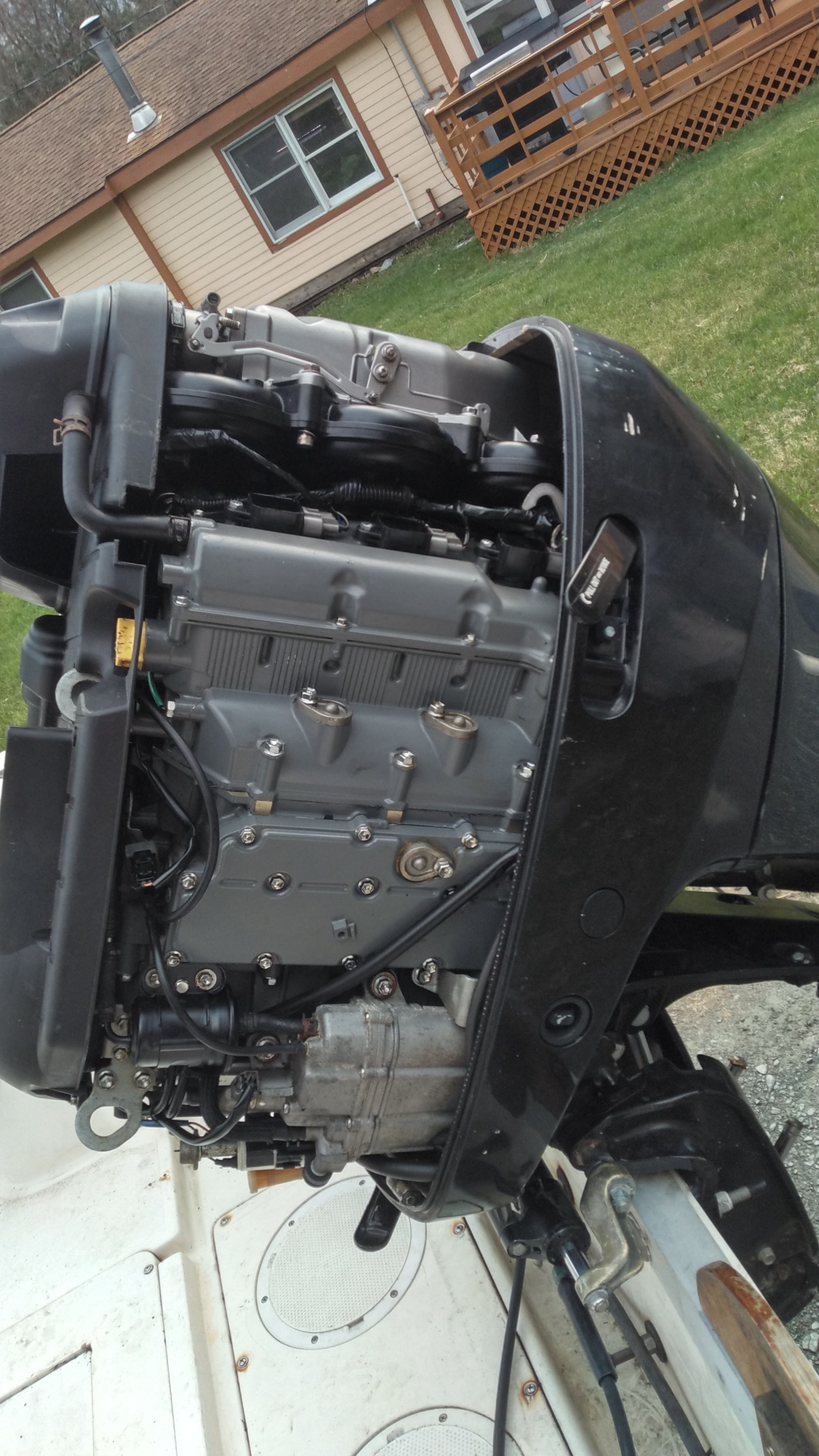 A close-up of a boat's outboard motor, with a house in the background.