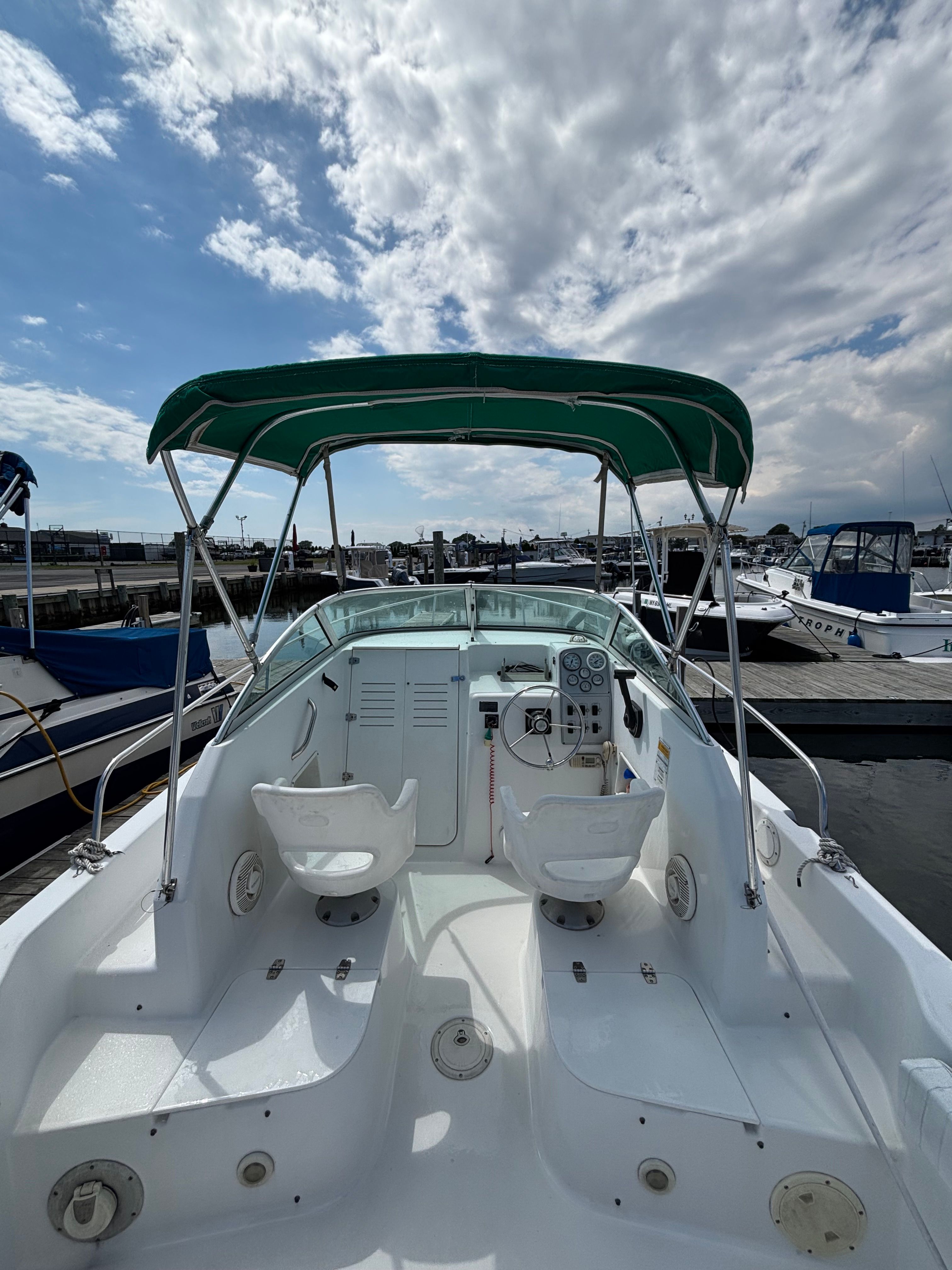 A 1999 Pro-Line 221 Walk Around boat with a green canopy, docked in a marina.