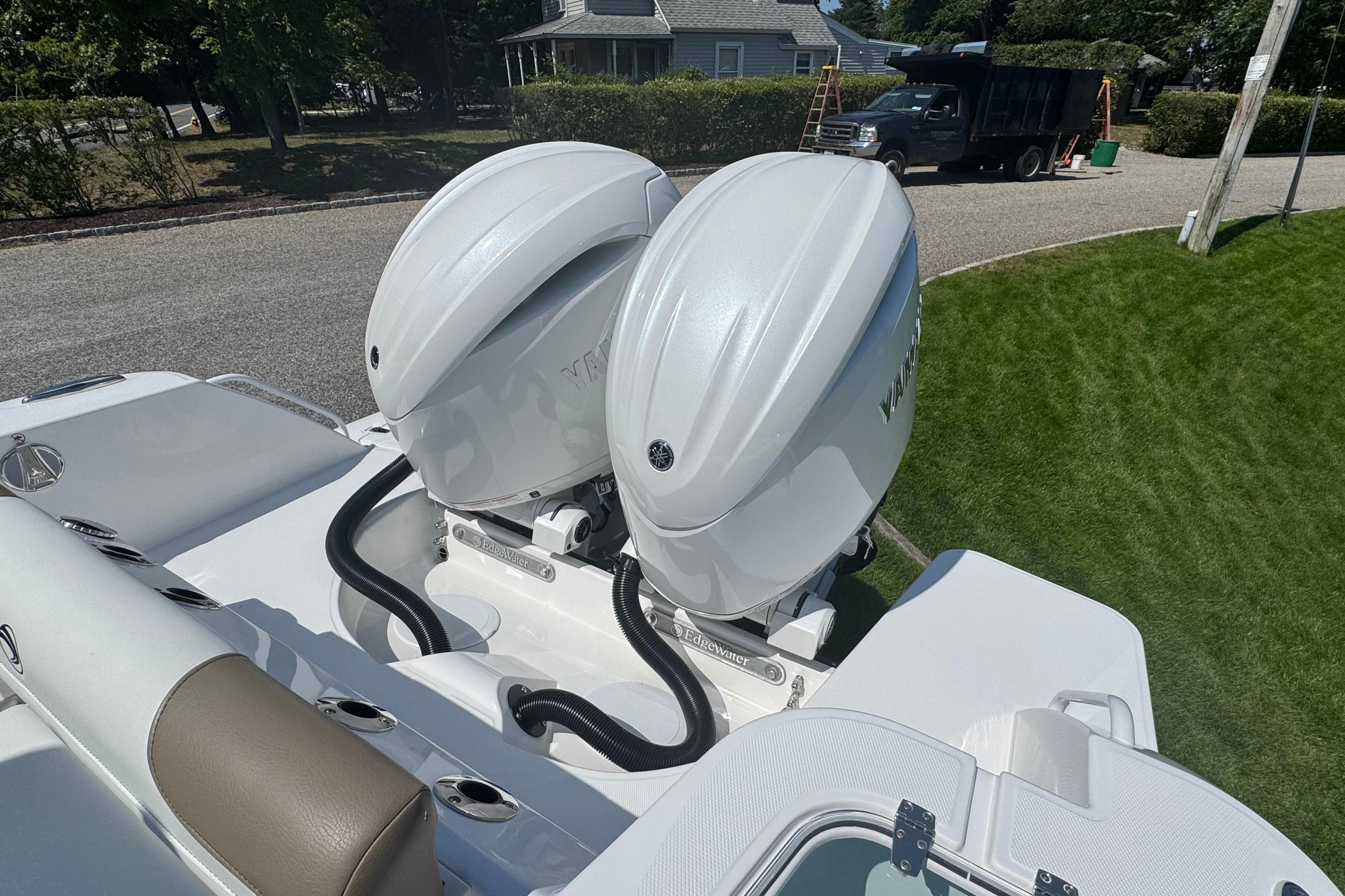 Twin outboard engines on a 2026 Edgewater 250CC boat, parked on a grassy area.
