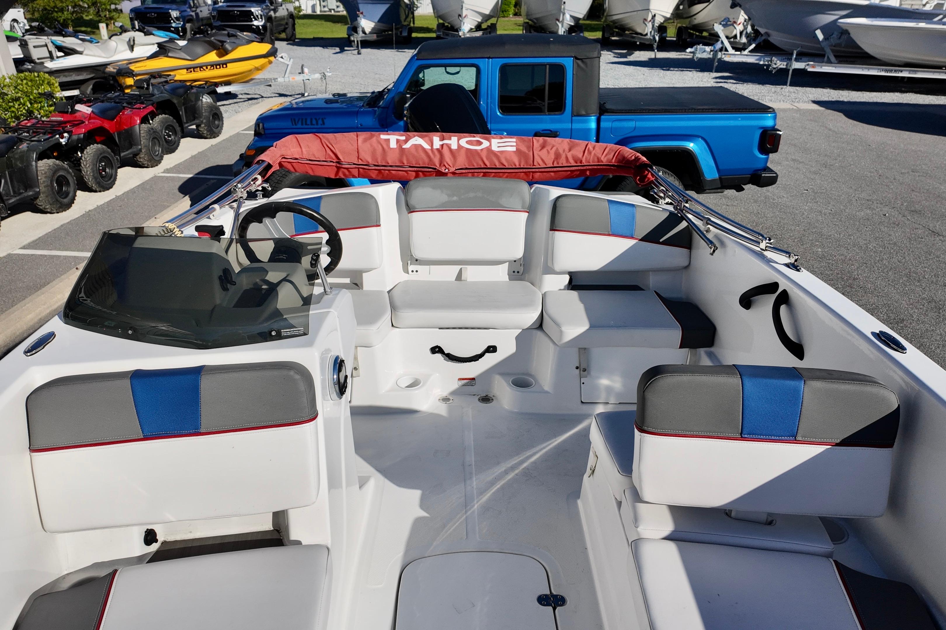 2024 Tahoe T18 boat interior with seating, steering wheel, and dashboard, parked near vehicles.