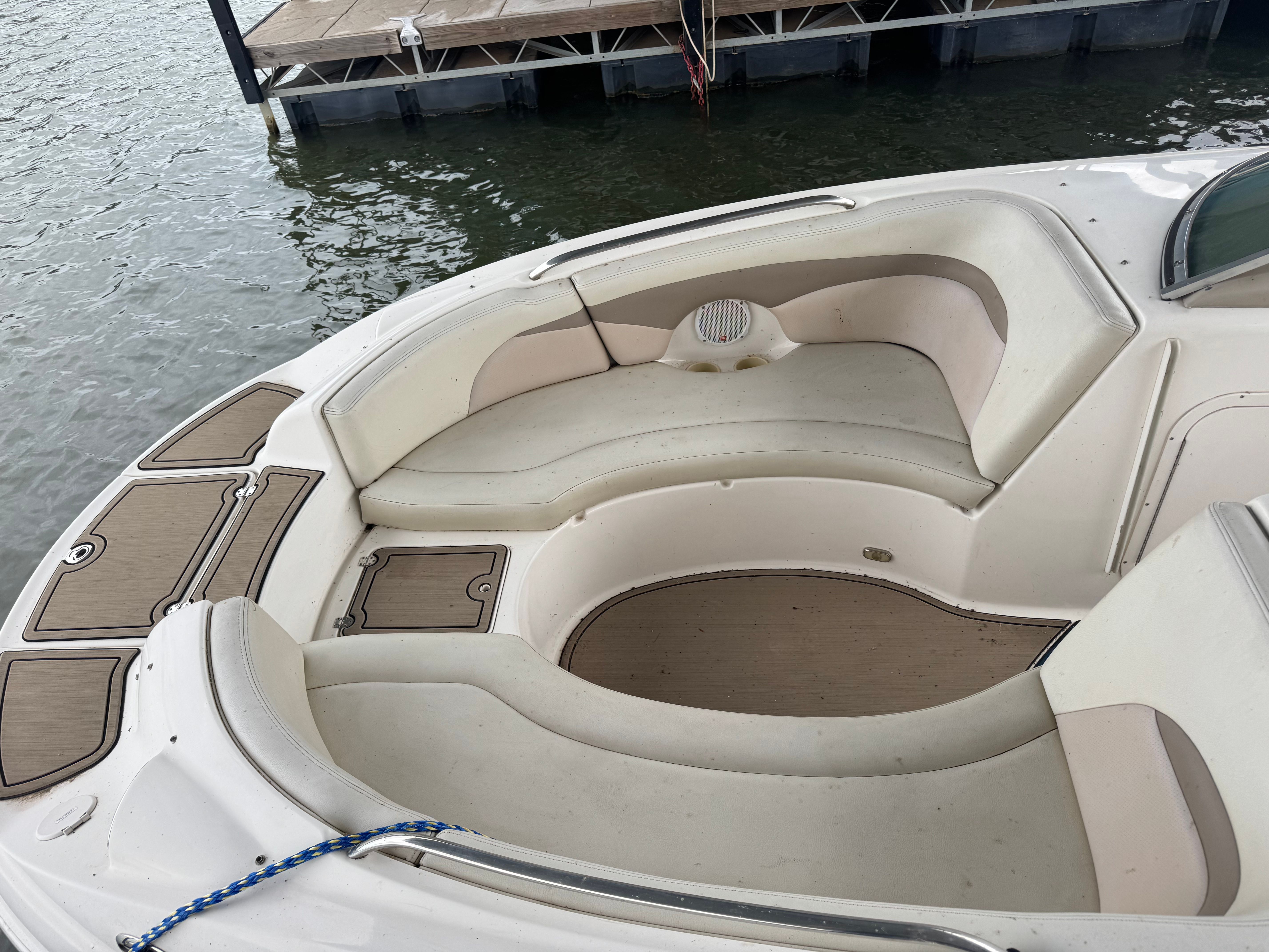A Chaparral Sunesta 223 boat with beige seating and a rounded seating area by the water.