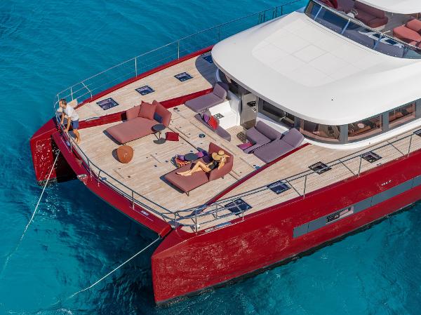 2025 Lagoon SIXTY 7 yacht with red exterior, spacious deck, and people relaxing on turquoise water.